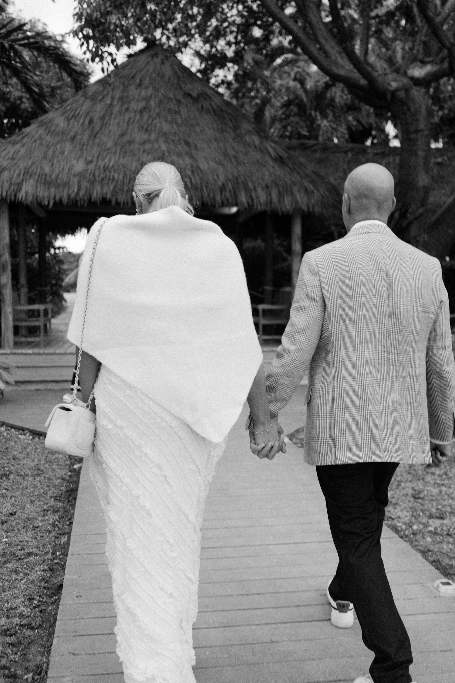Two people walking together on a wooden boardwalk in formal attire.