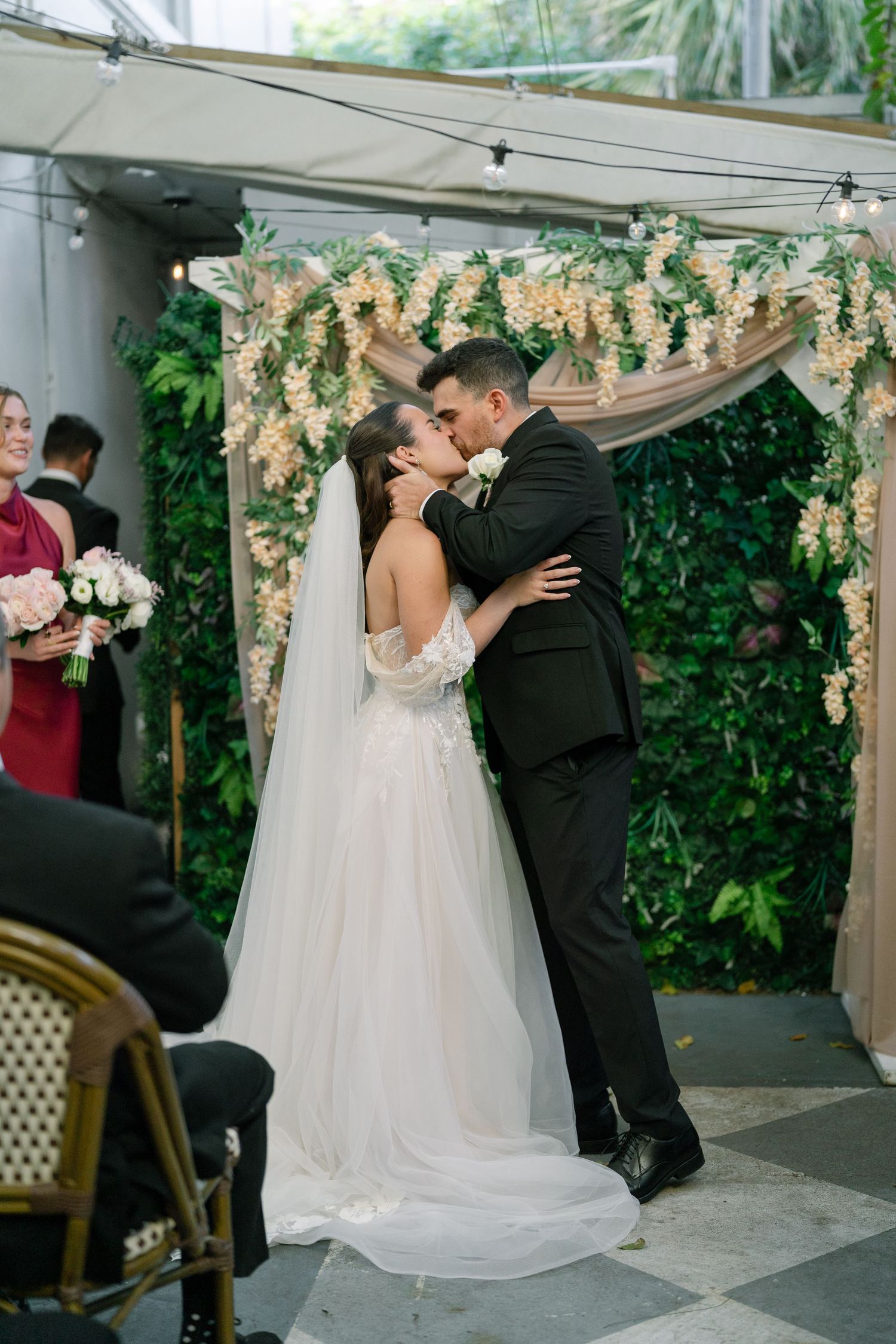 Bride and groom share their first kiss under a floral arch at their wedding ceremony.