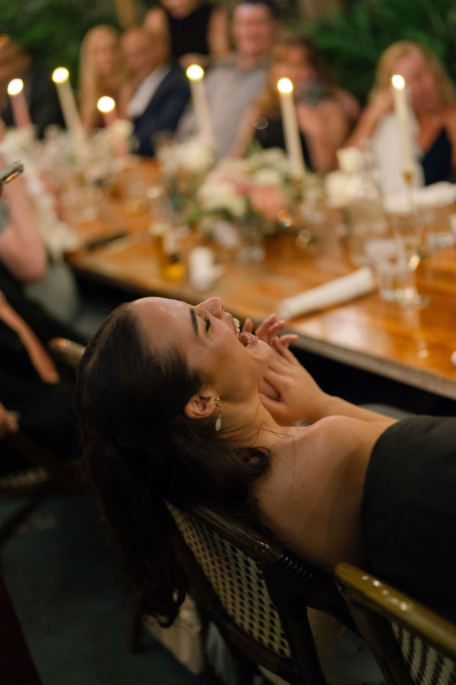 Wedding guest laughing joyfully at a candlelit dinner reception table surrounded by guests.