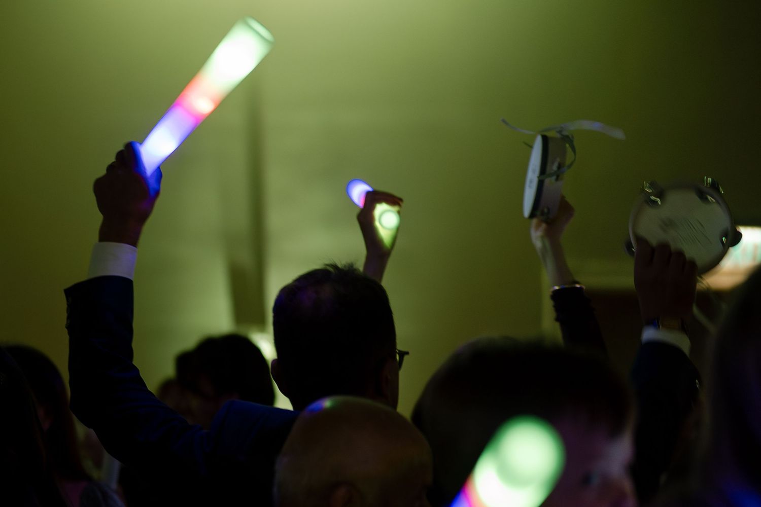 Silhouettes of crowd with raised hands against dark background with colorful stage lighting.