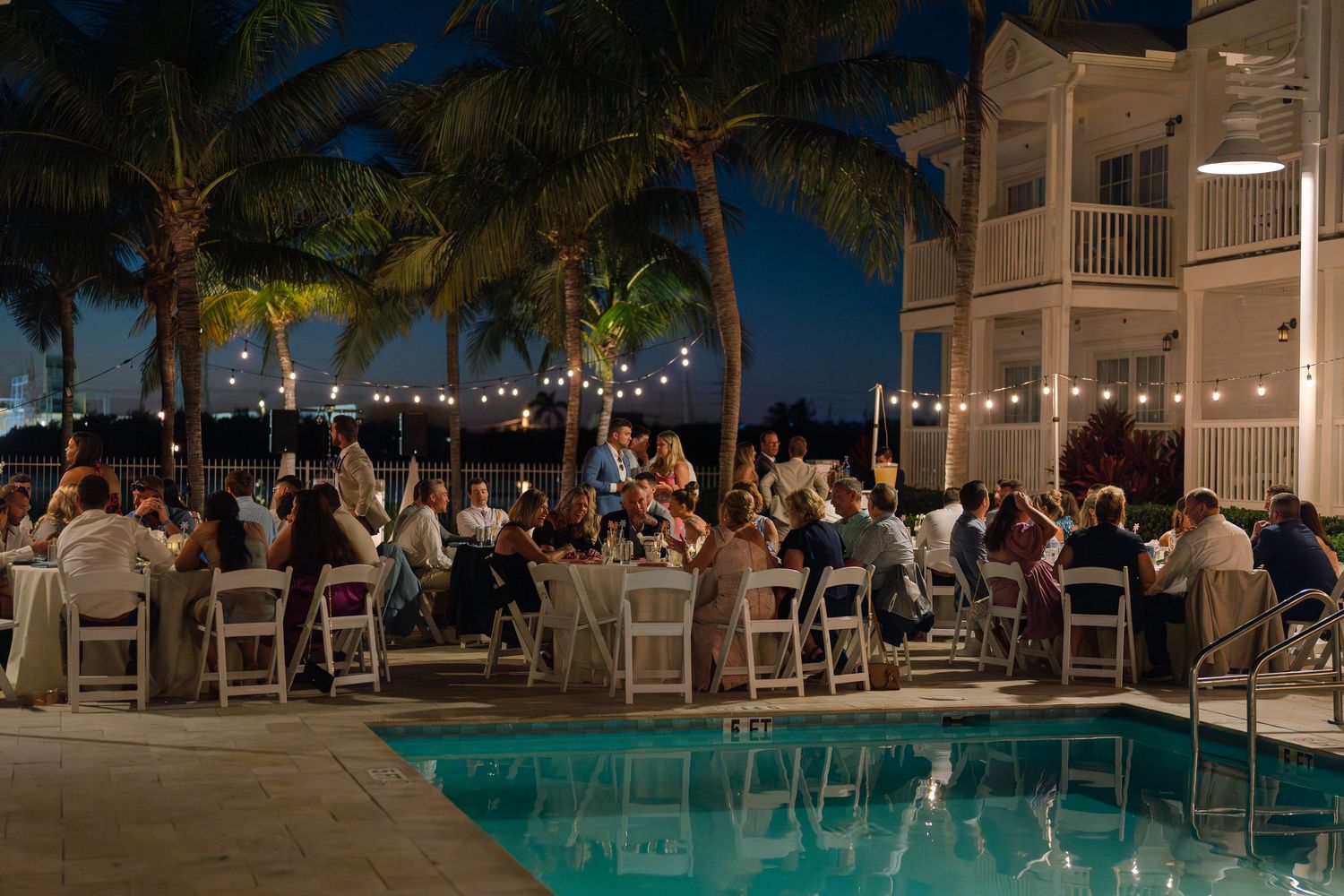 Evening wedding reception by a pool with string lights and palm trees creating a romantic ambiance.