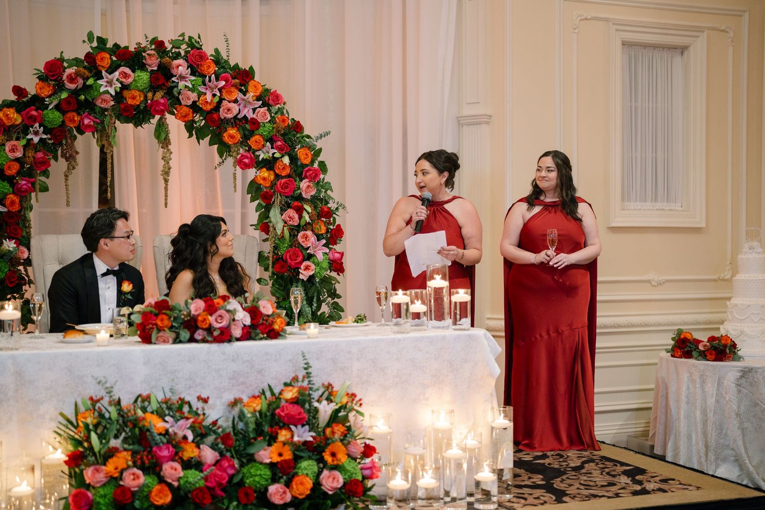 Wedding reception venue decorated with red and pink floral arrangements and white candles.