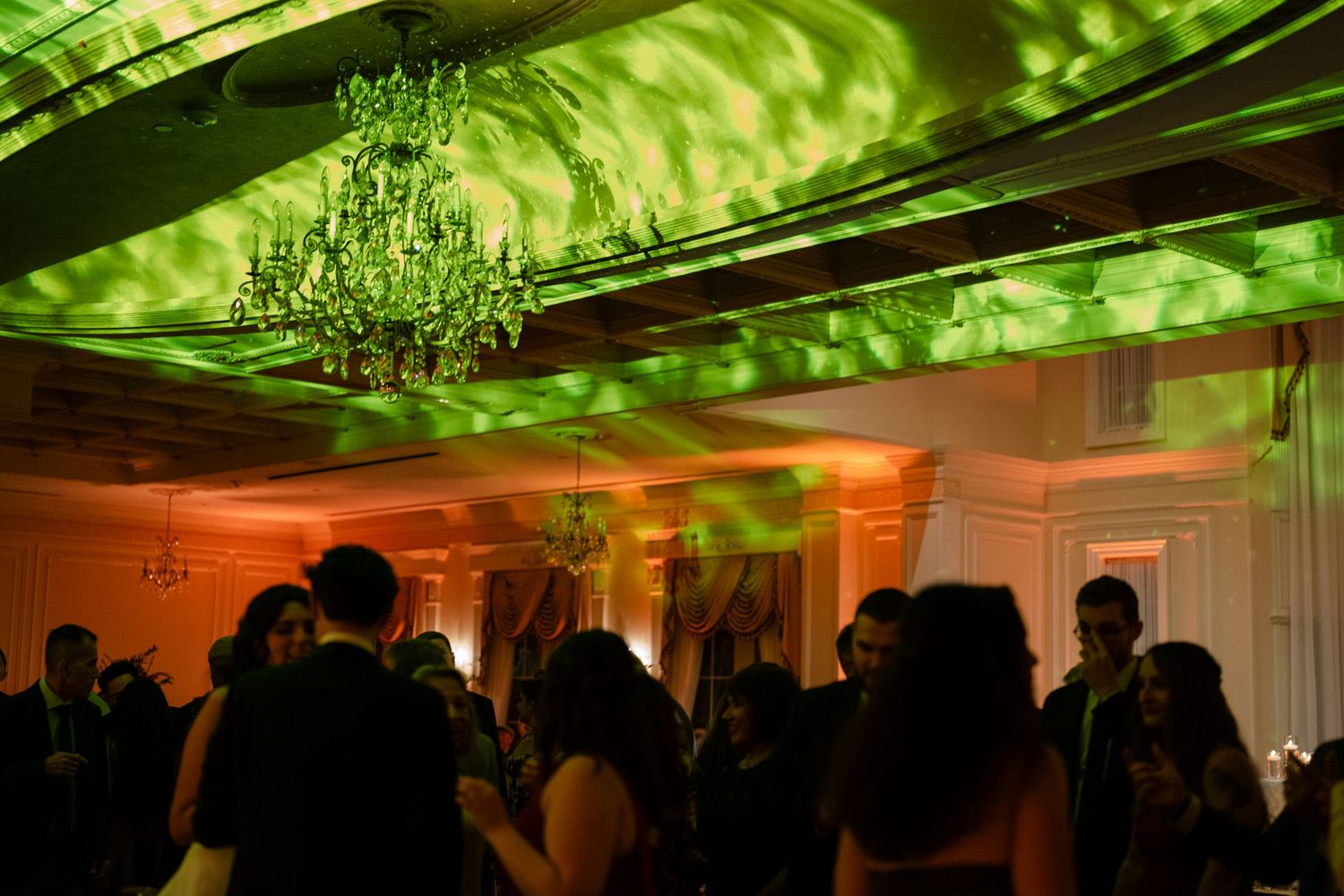 A wedding reception dance floor illuminated with dramatic green lighting and a crystal chandelier.