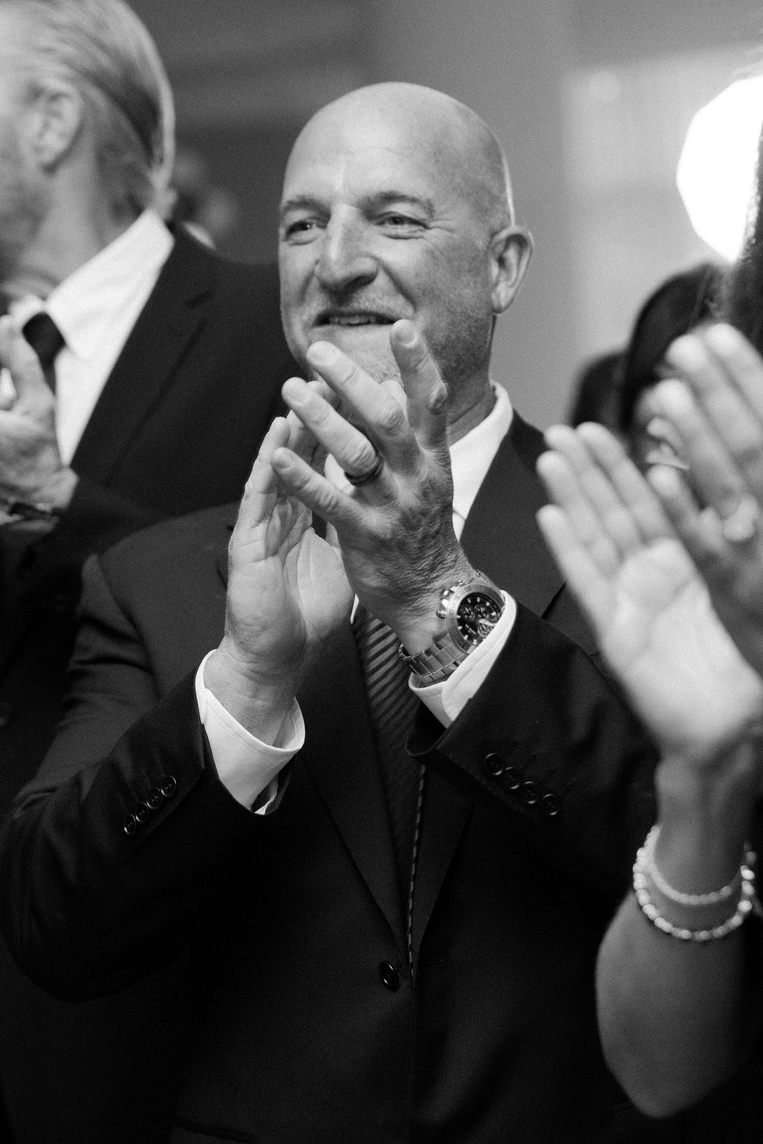 A well-dressed guest in a suit applauds enthusiastically during a formal event.