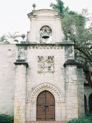 Historic stone church entrance with ornate bell tower, arched wooden door, and decorative architectural details in Spanish colonial style.