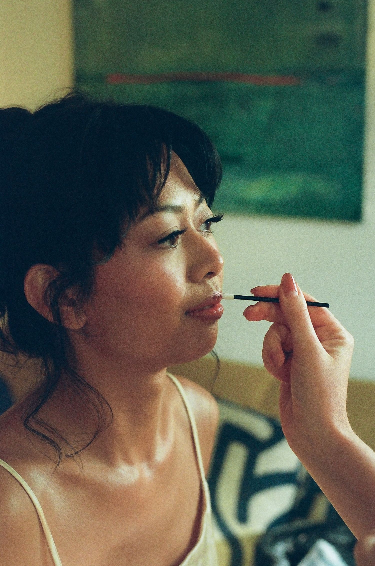 A woman having lip makeup applied with a brush by a makeup artist in a bright room.
