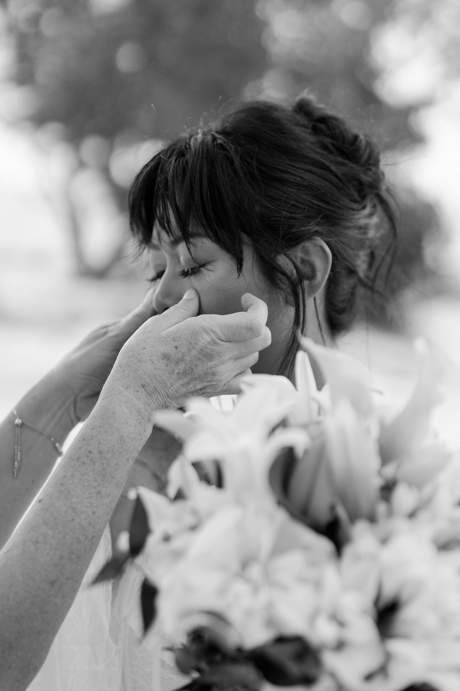 Black and white photo of an emotional bride crying while holding a bouquet of lilies on her wedding day.