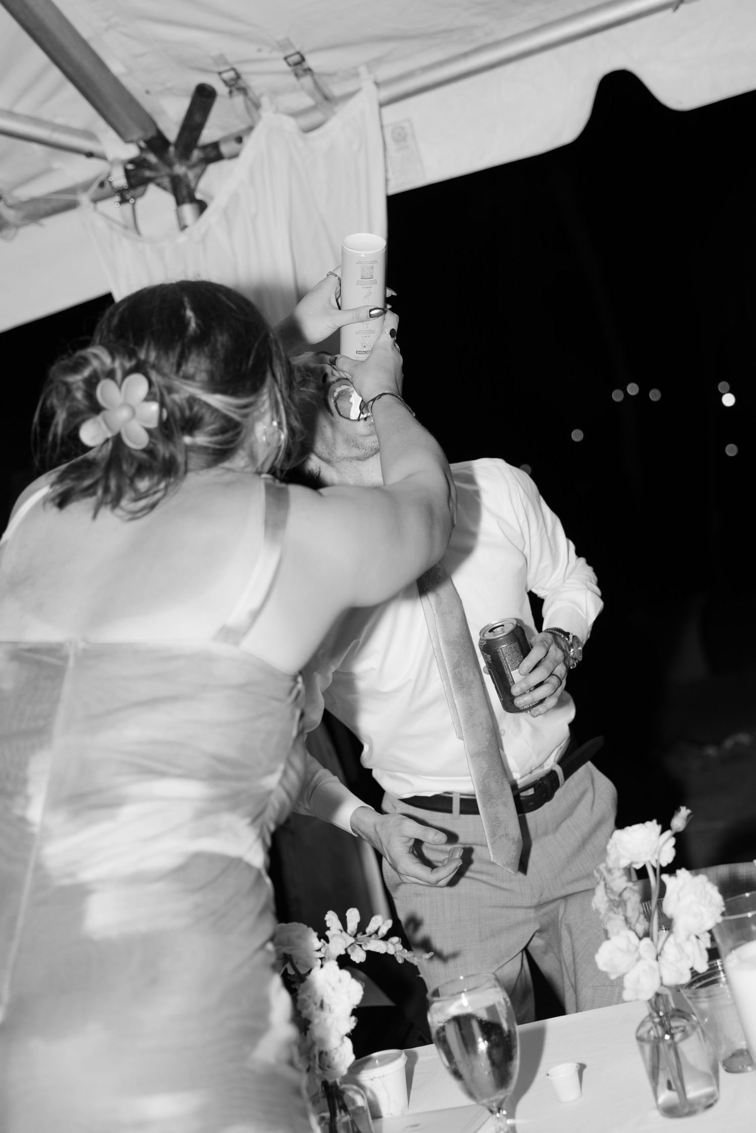 Black and white photo of bride and groom sharing a dance at outdoor wedding reception under tent at night.