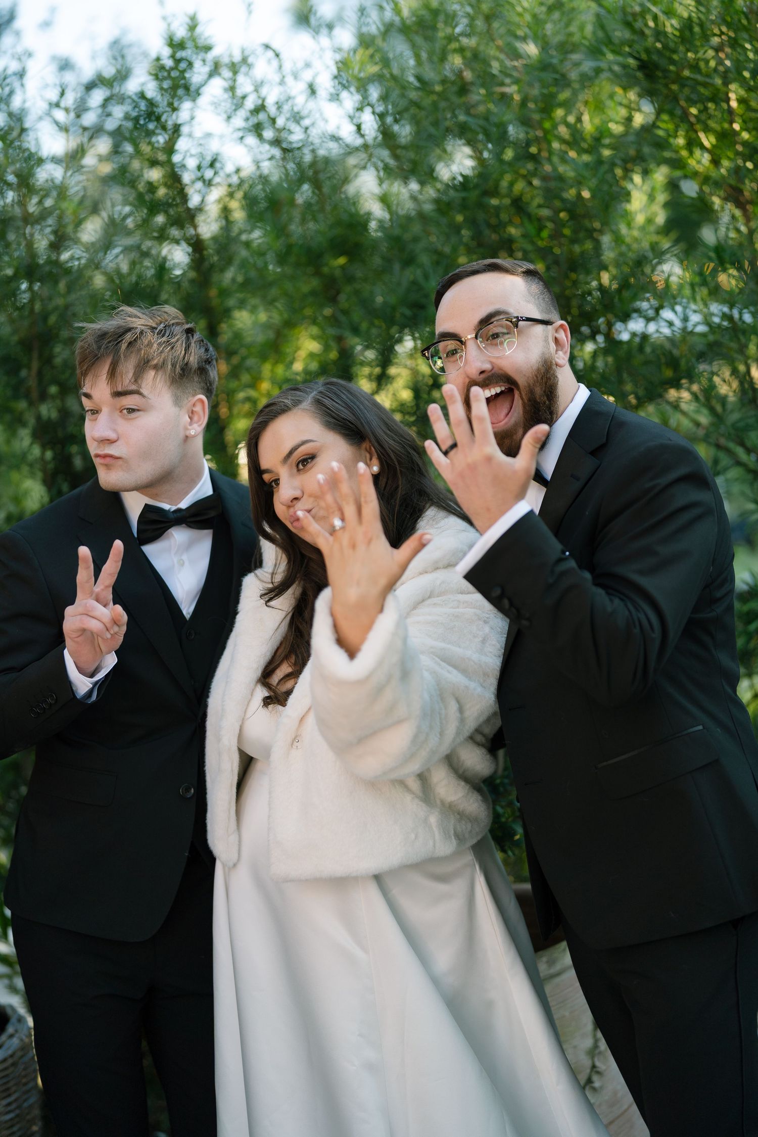 A group of people in formal attire making funny faces and gestures in a garden setting.