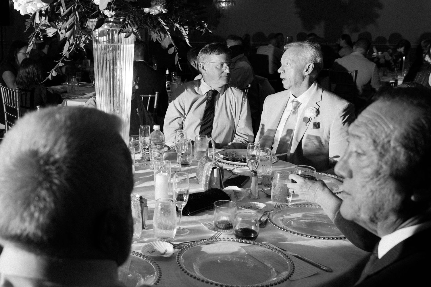 A black and white photograph shows a group of people seated at a formal dinner table in what appears to be the 1950s.