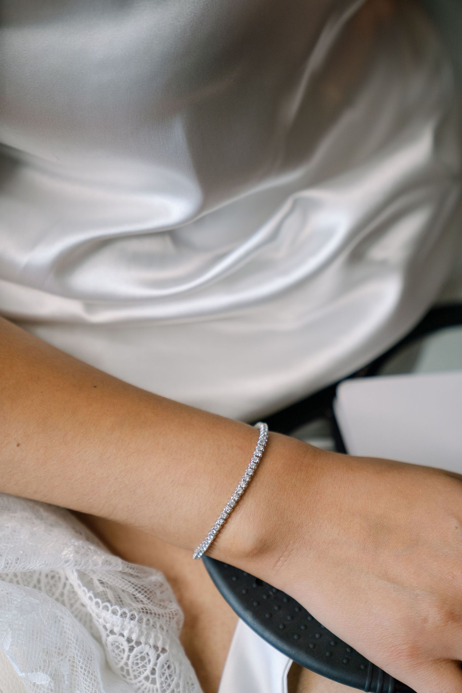 Close-up of a delicate lace sleeve and diamond bracelet on a bride's wrist.