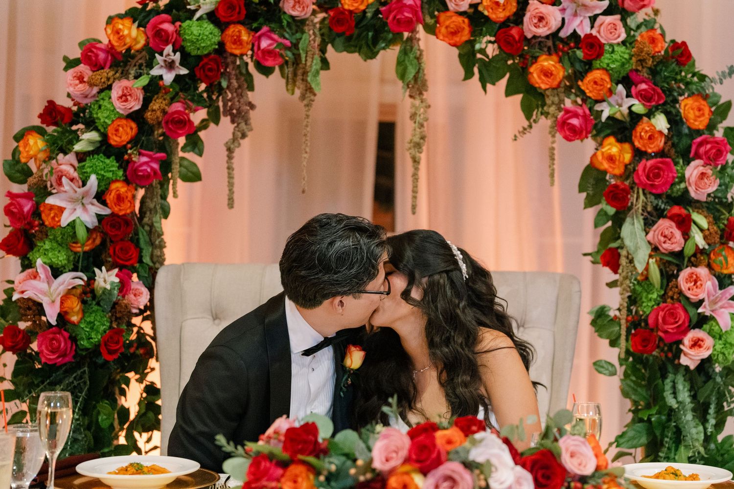 Elegant floral arrangements with red, orange and pink flowers decorate the ceiling at a formal event venue.