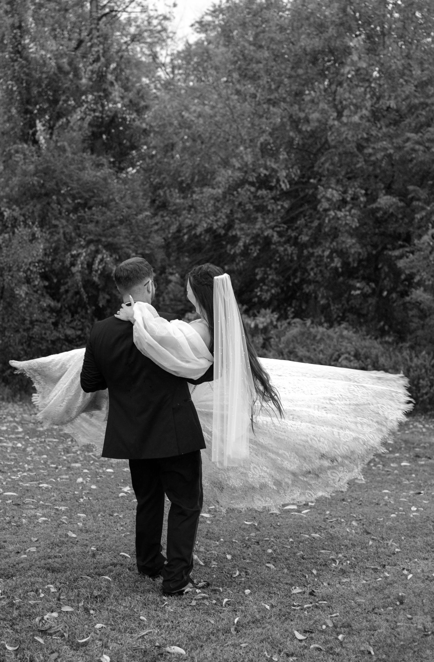 Black and white photo of a couple dancing playfully in an outdoor garden setting.