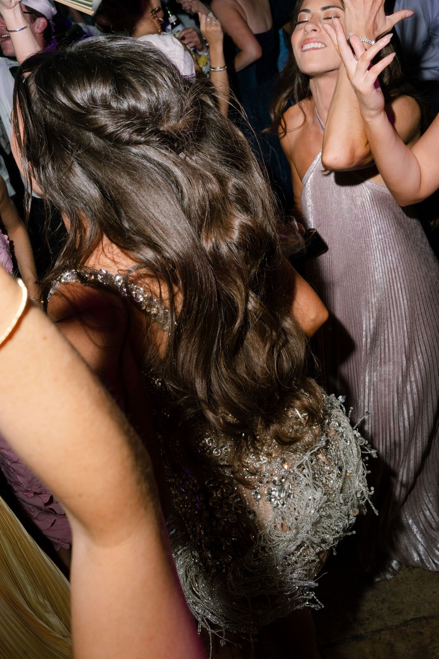 Close-up of bride with long wavy hair in beaded gown dancing at wedding reception.
