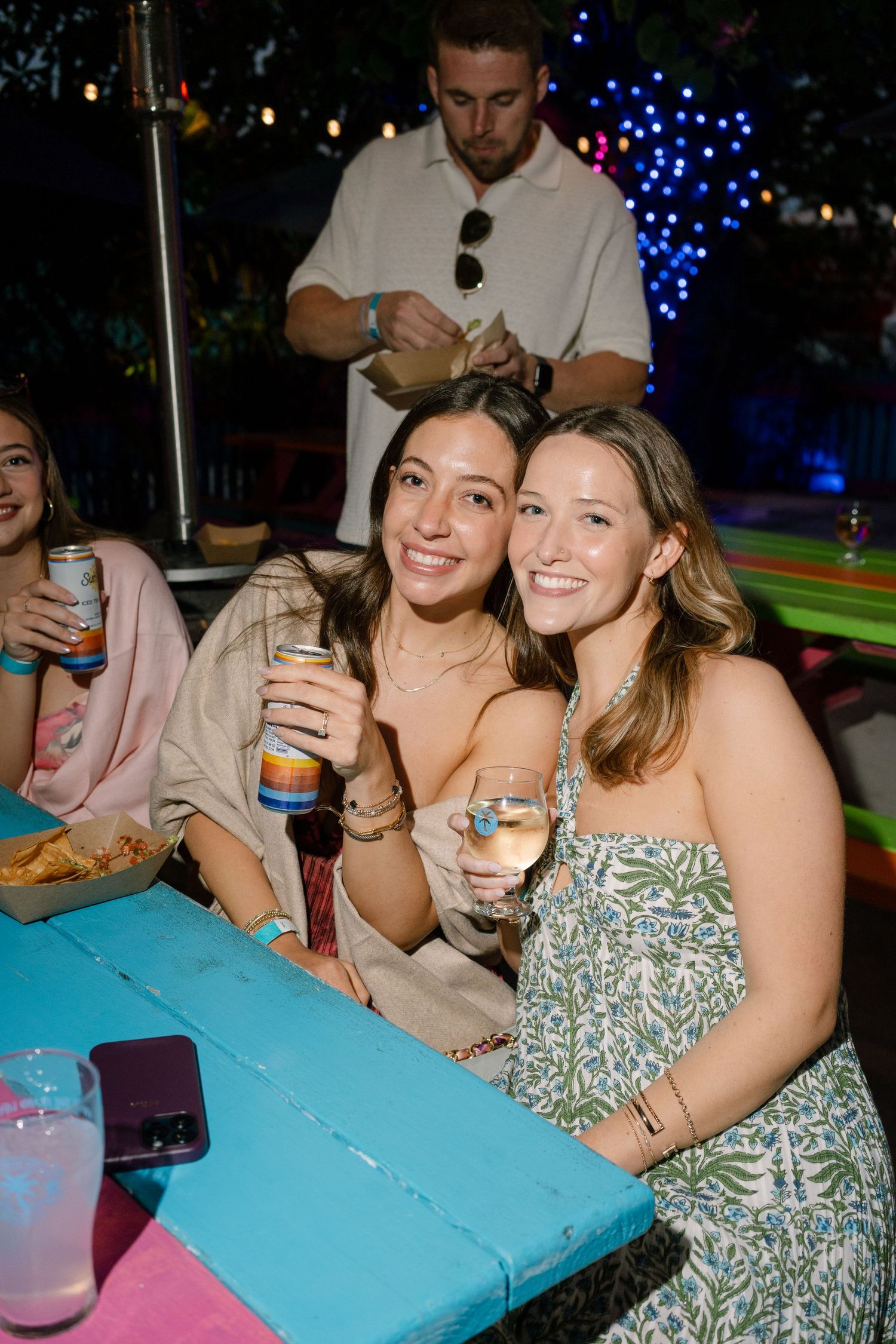 Friends enjoying drinks and snacks at an outdoor party with festive lighting.