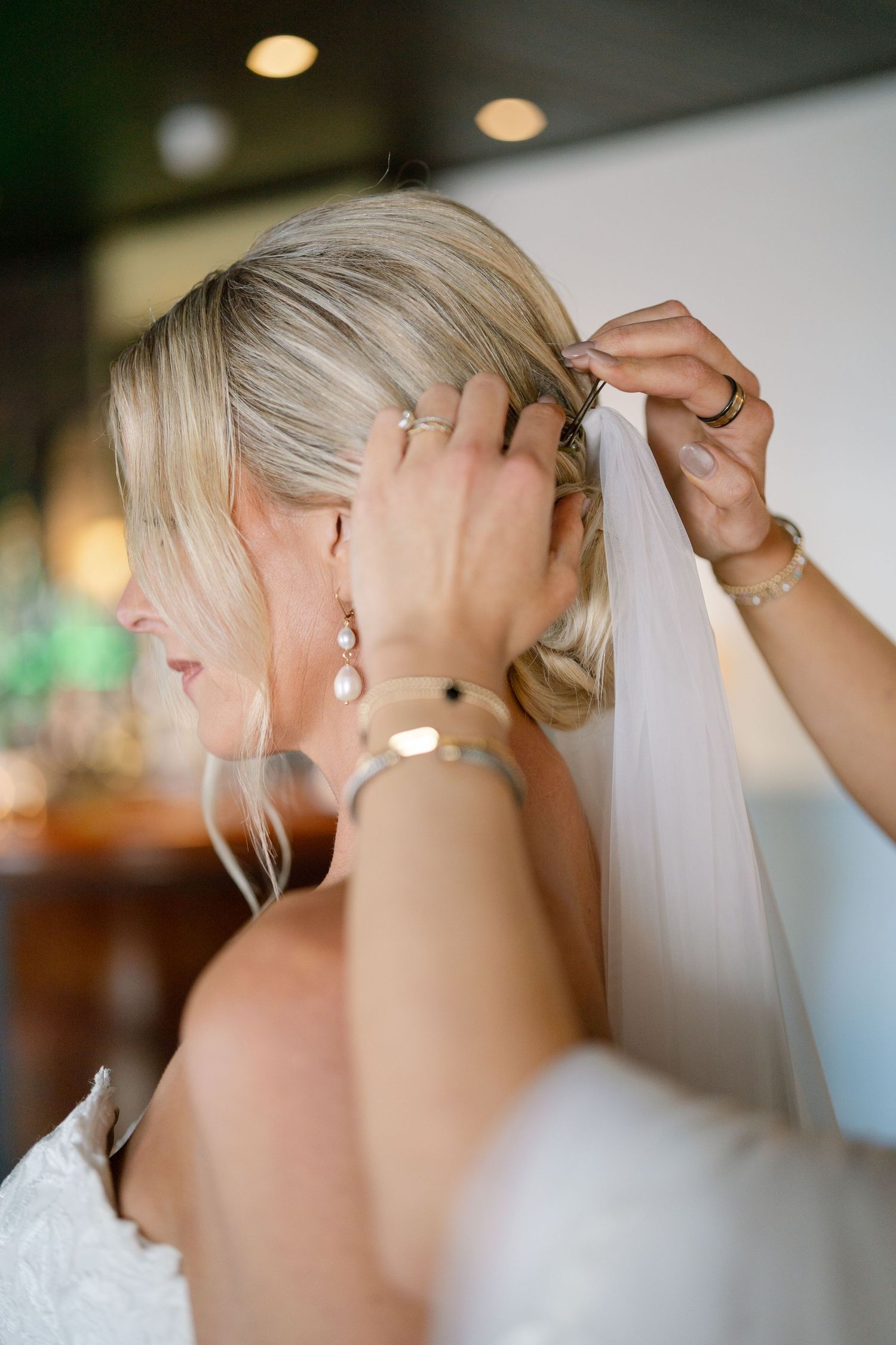 Close-up sequence showing a wedding veil being carefully attached to a blonde updo hairstyle with pearl earrings.