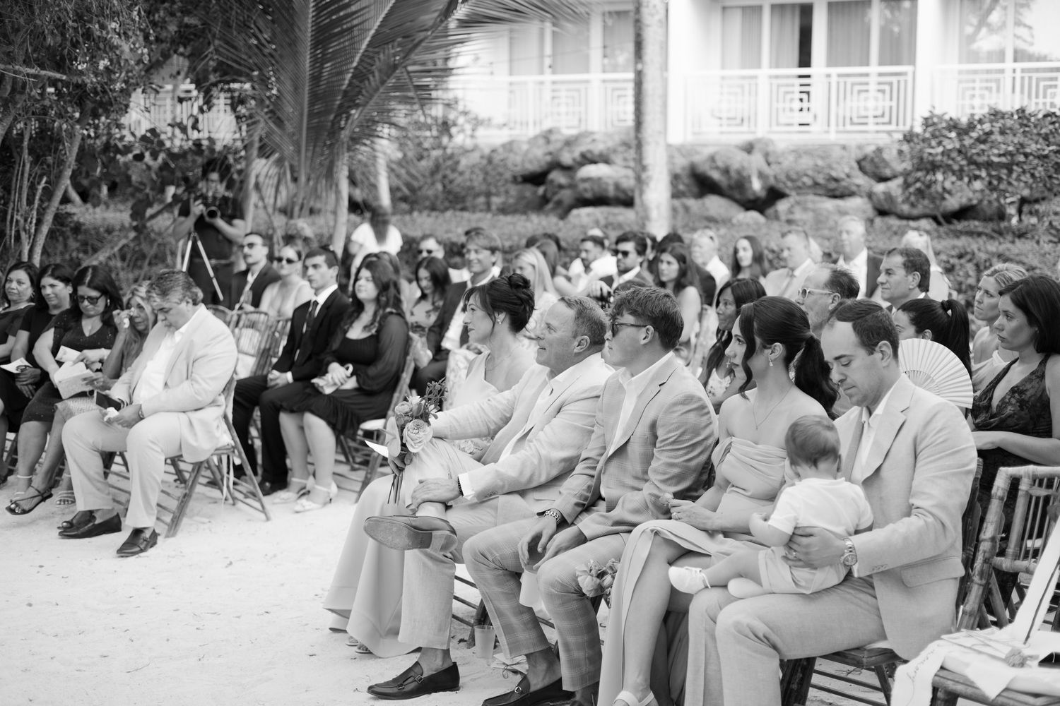 Black and white photo of wedding guests seated in rows at an outdoor ceremony.