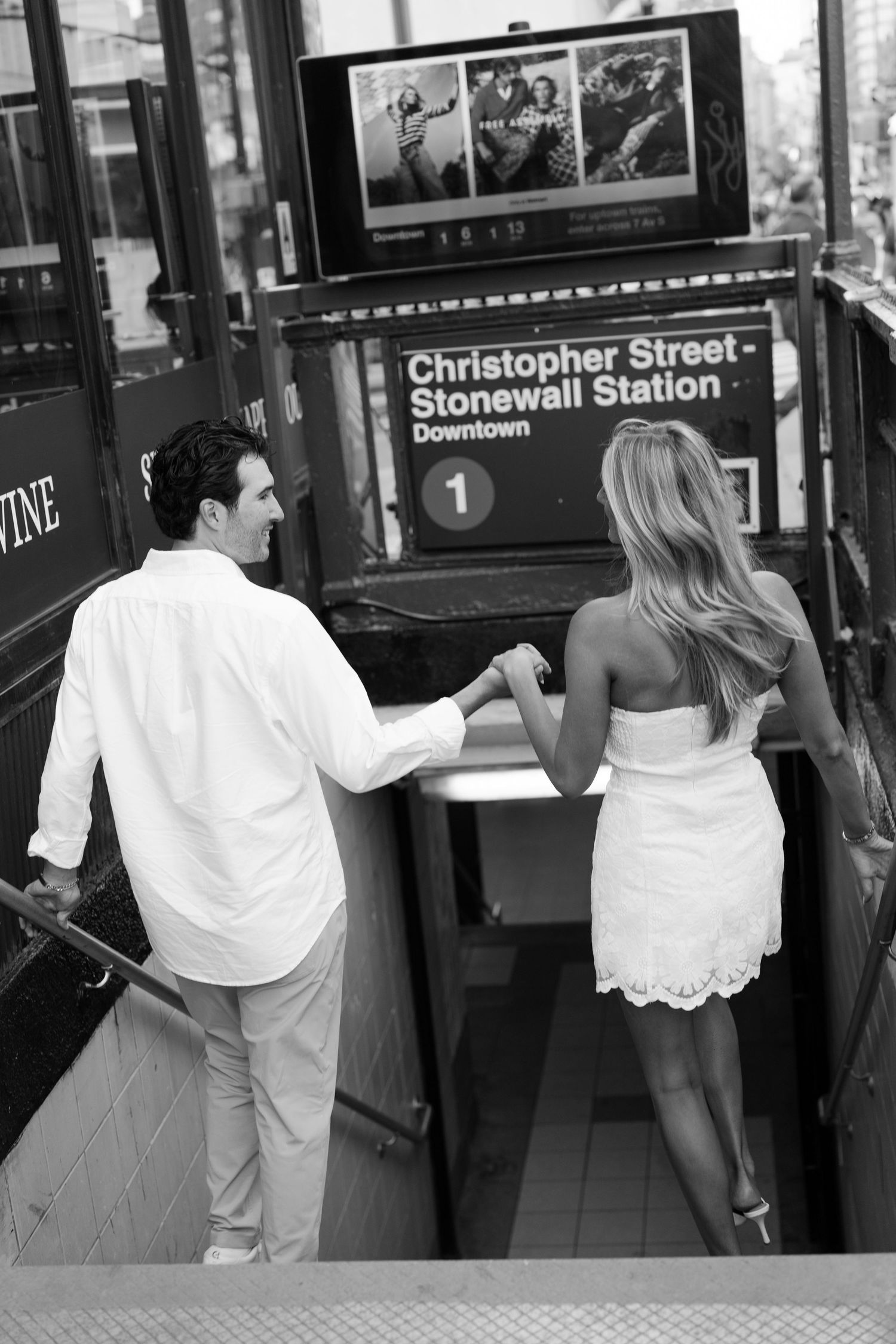 Couple in white holding hands descending into Christopher Street Stonewall Station subway entrance in NYC.