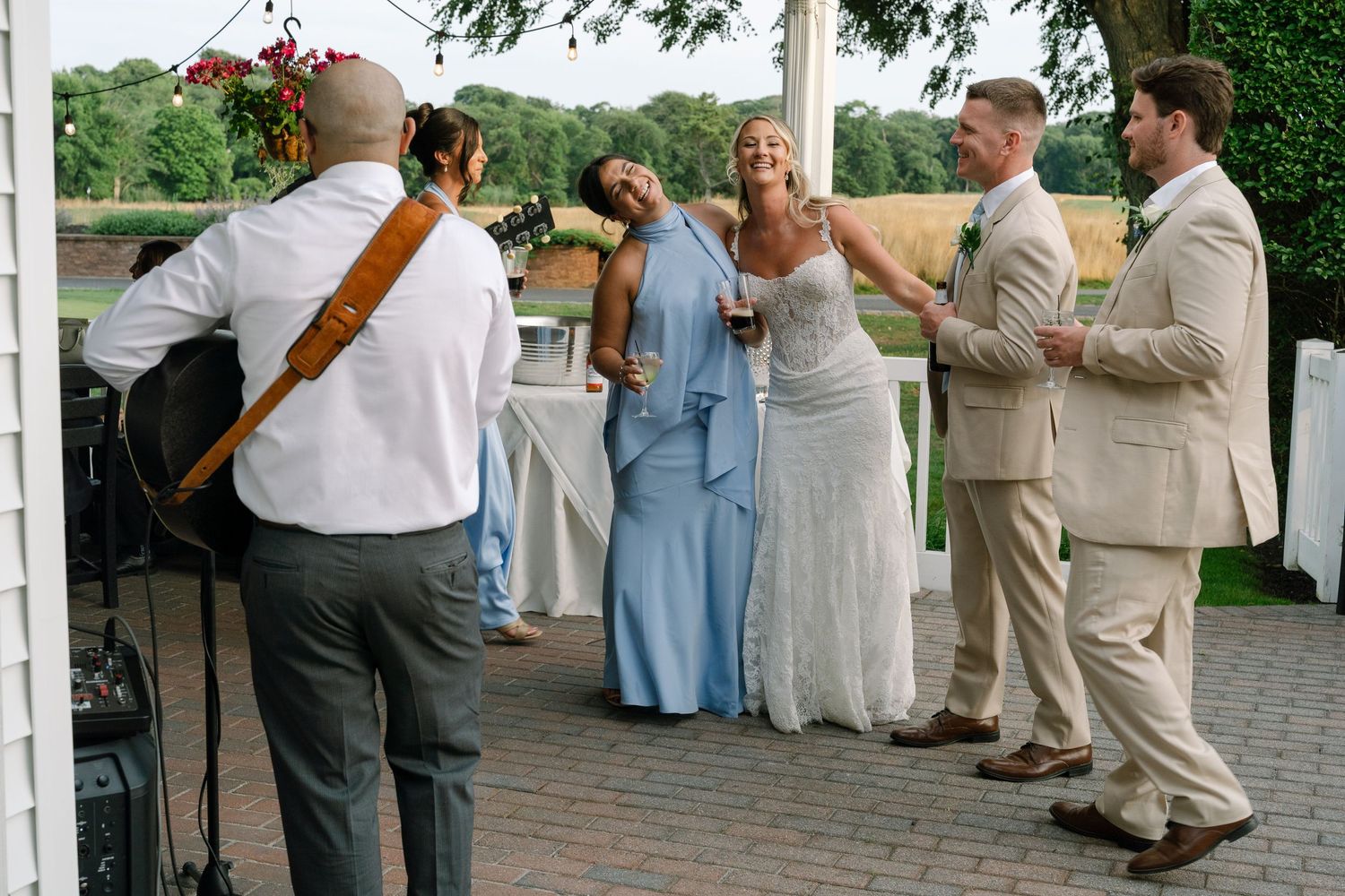 Wedding guests dance and celebrate as a guitarist performs at an outdoor reception venue near a waterfront.
