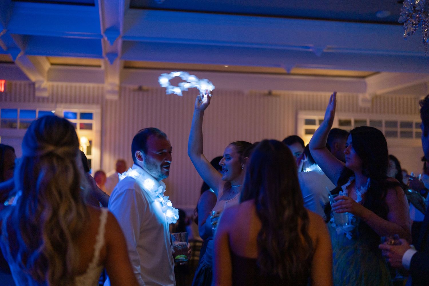 Wedding guests dancing under blue lights at lively indoor reception celebration.