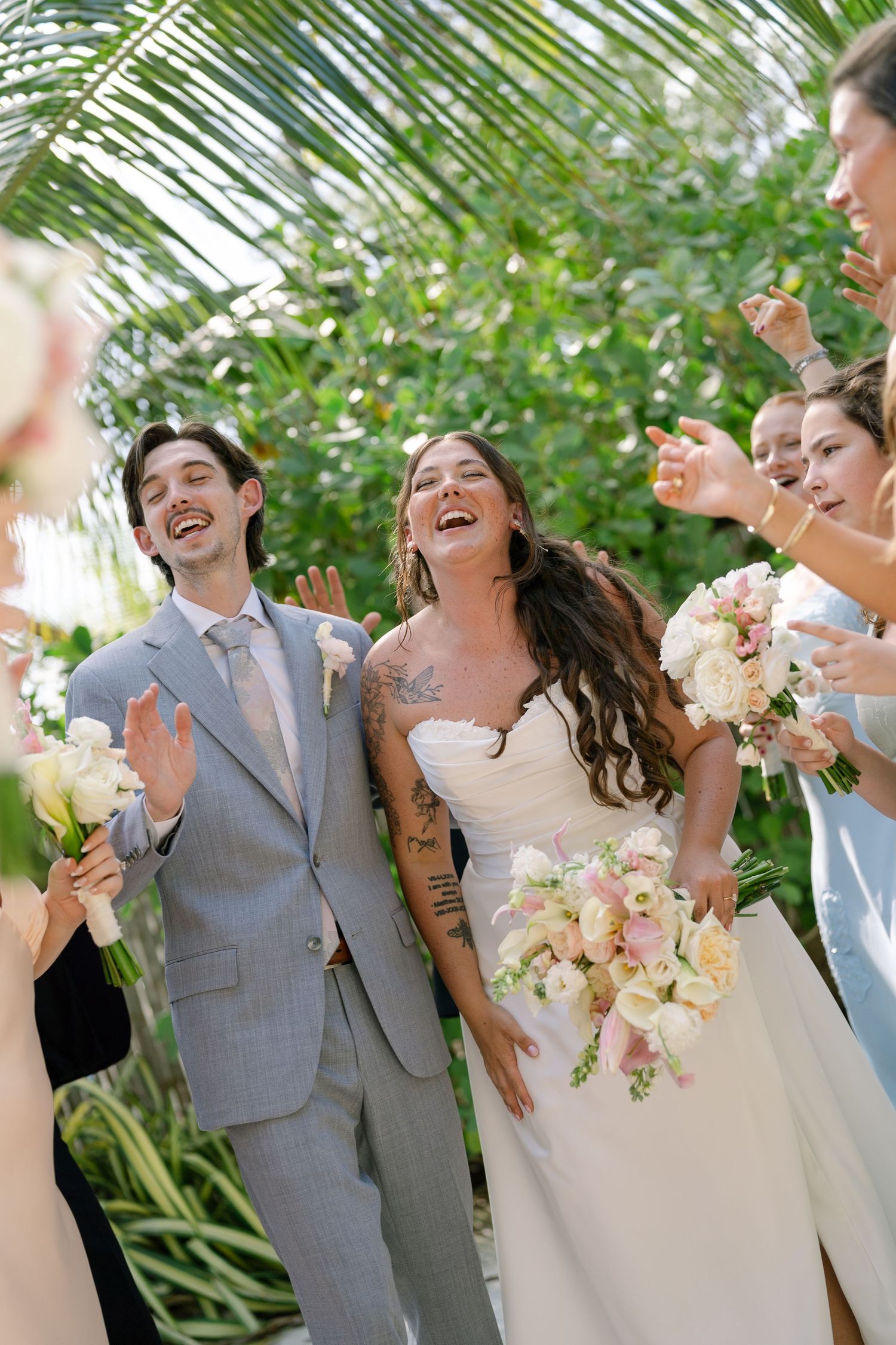 A bride and groom walk together surrounded by their wedding party, with lush greenery in the background.
