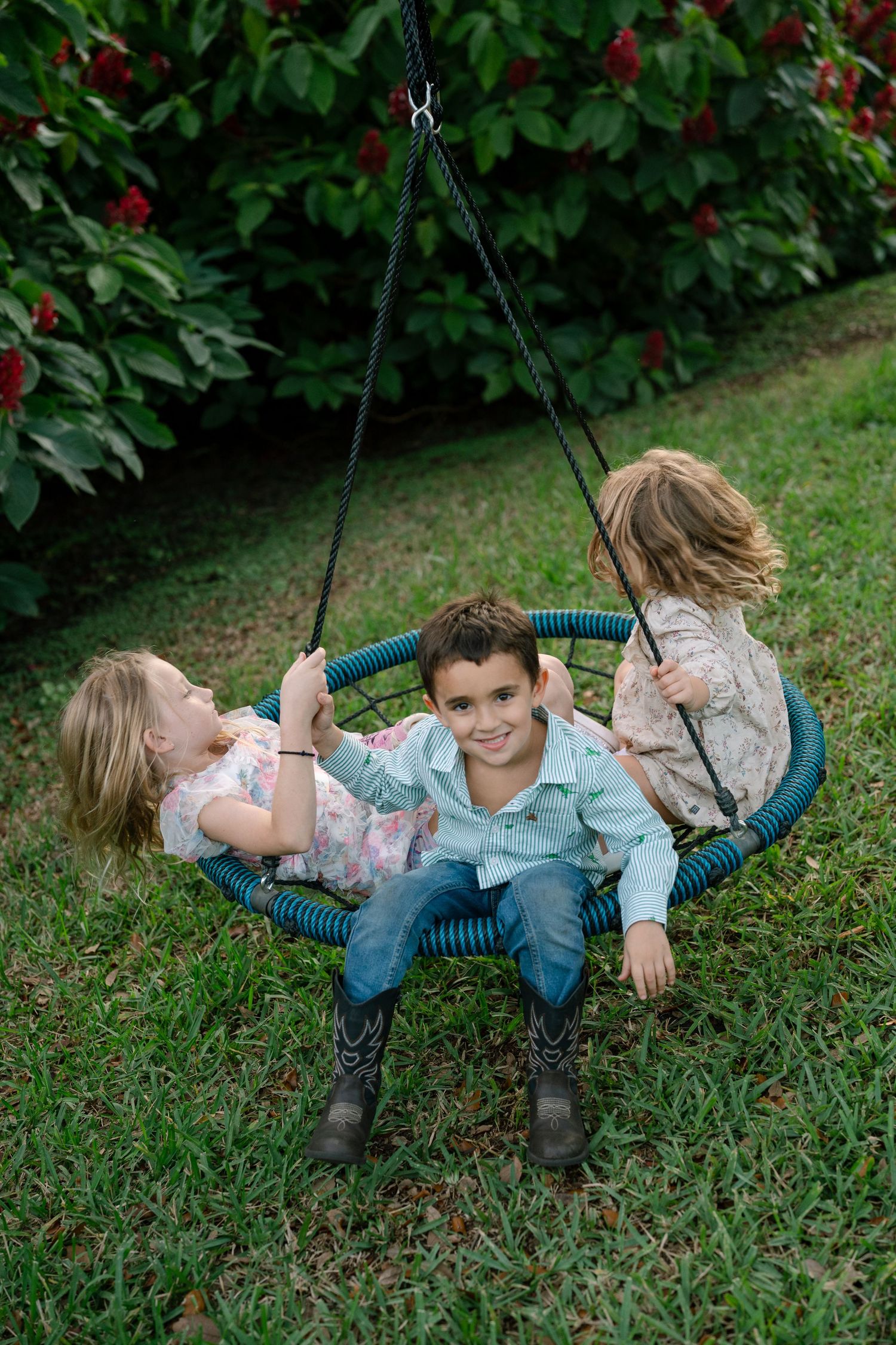 Children playing together on a round rope swing in a garden setting.
