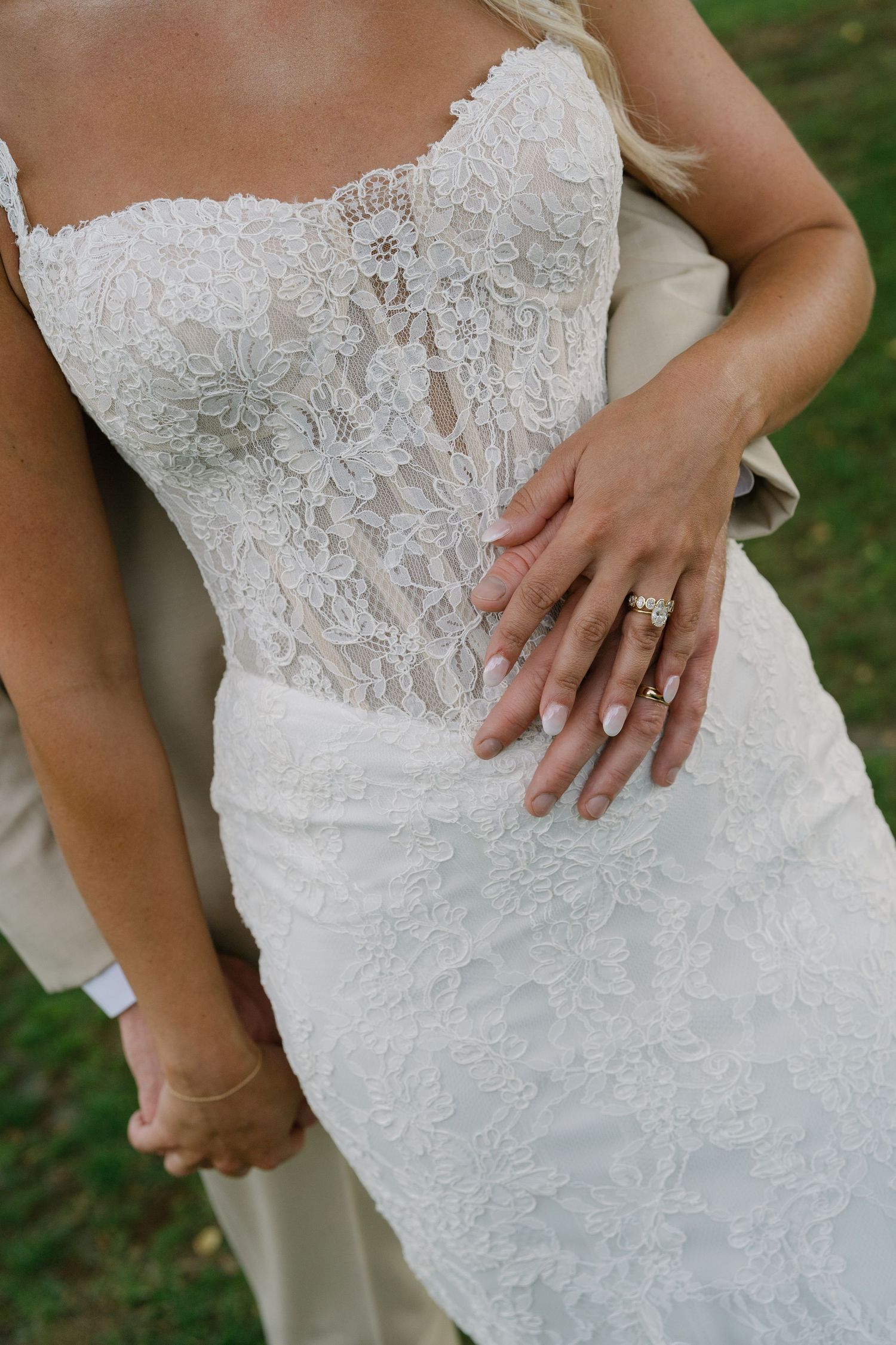 Close-up of bride in fitted lace wedding gown with groom's hand resting on her waist.