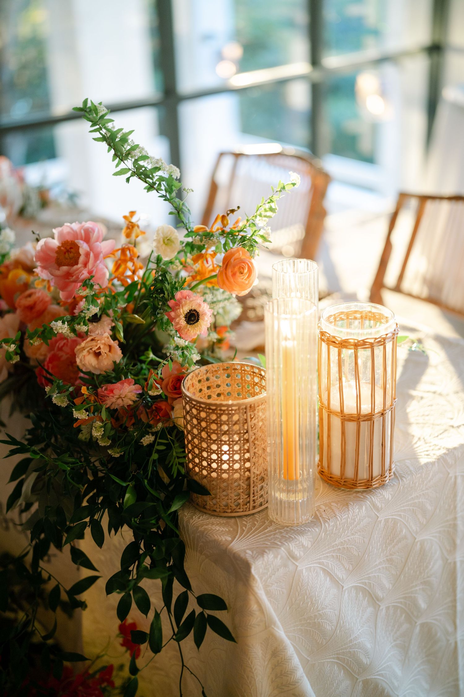 Elegant table setting with pink floral arrangements and glowing glass candle holders on white textured tablecloth.