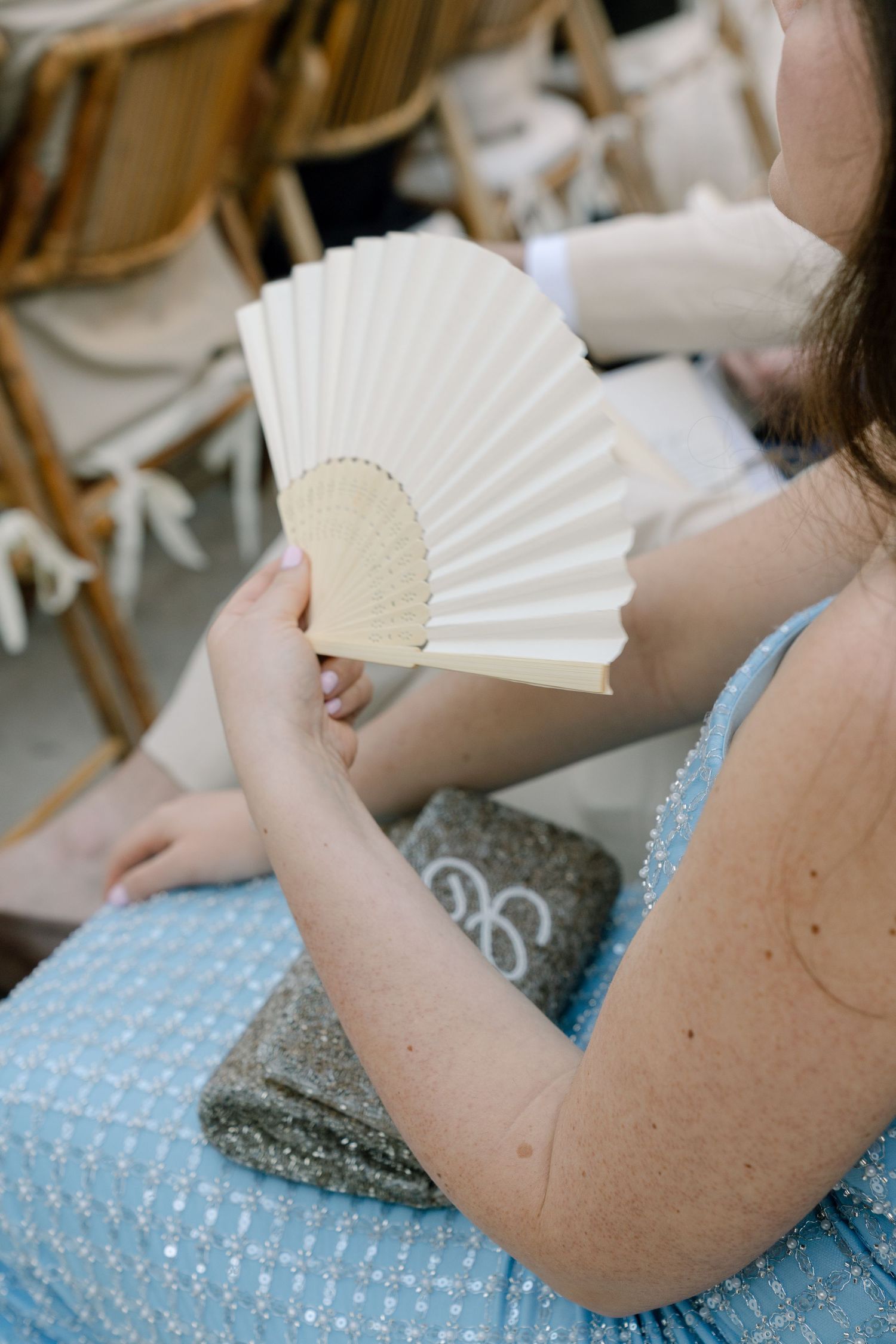 A guest in a polka dot dress holds a white paper fan while seated in a wooden chair.