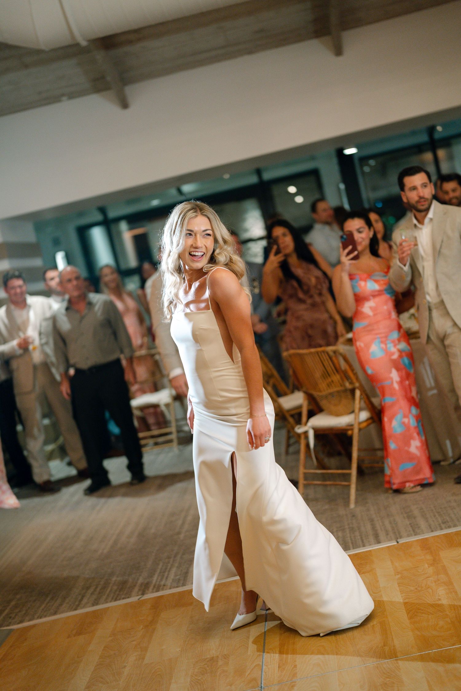 Wedding guests dancing and celebrating on a wooden dance floor at an indoor reception.
