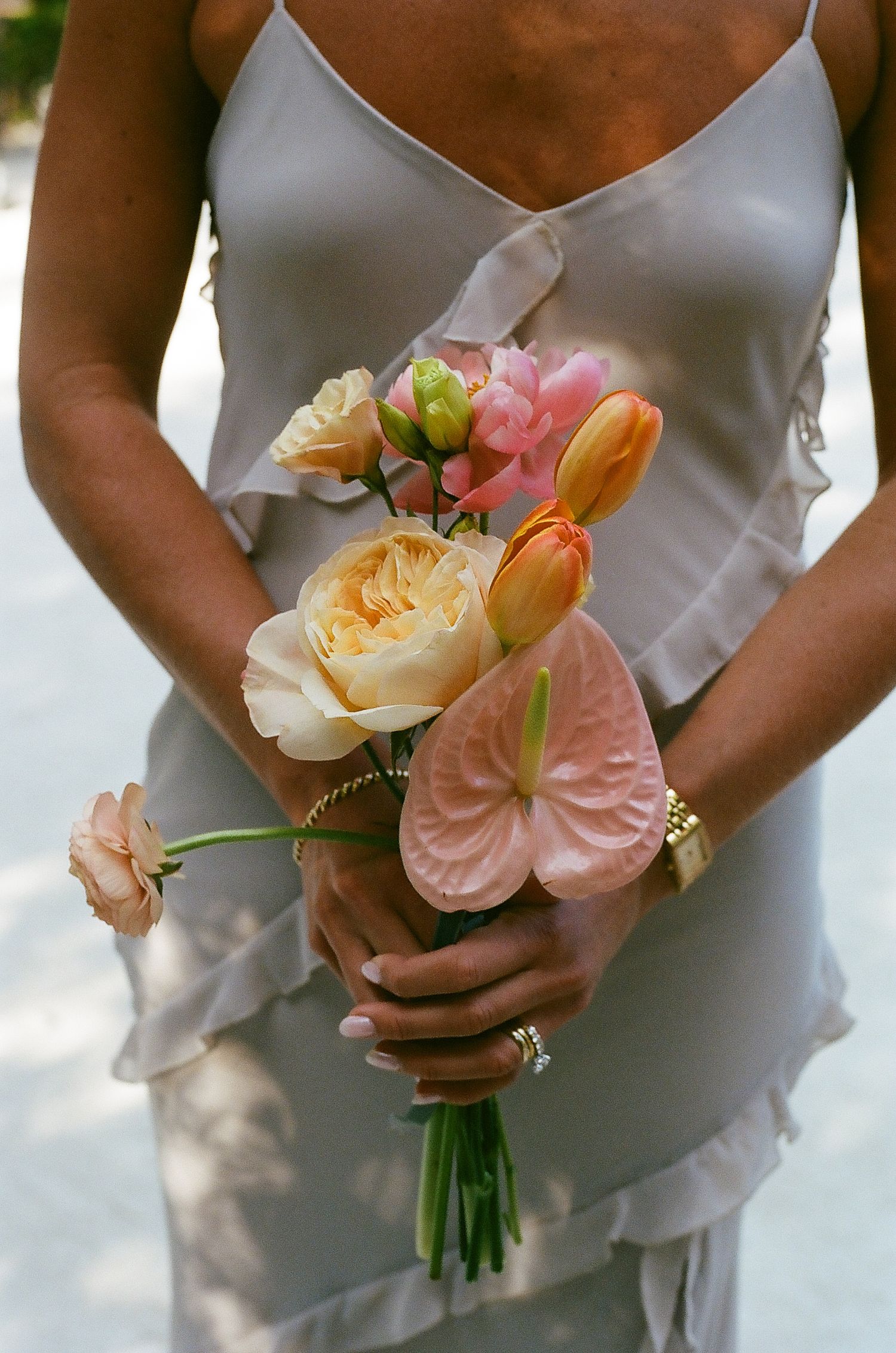 Close-up series of bridesmaids holding delicate peach and pink floral bouquets against white dresses.