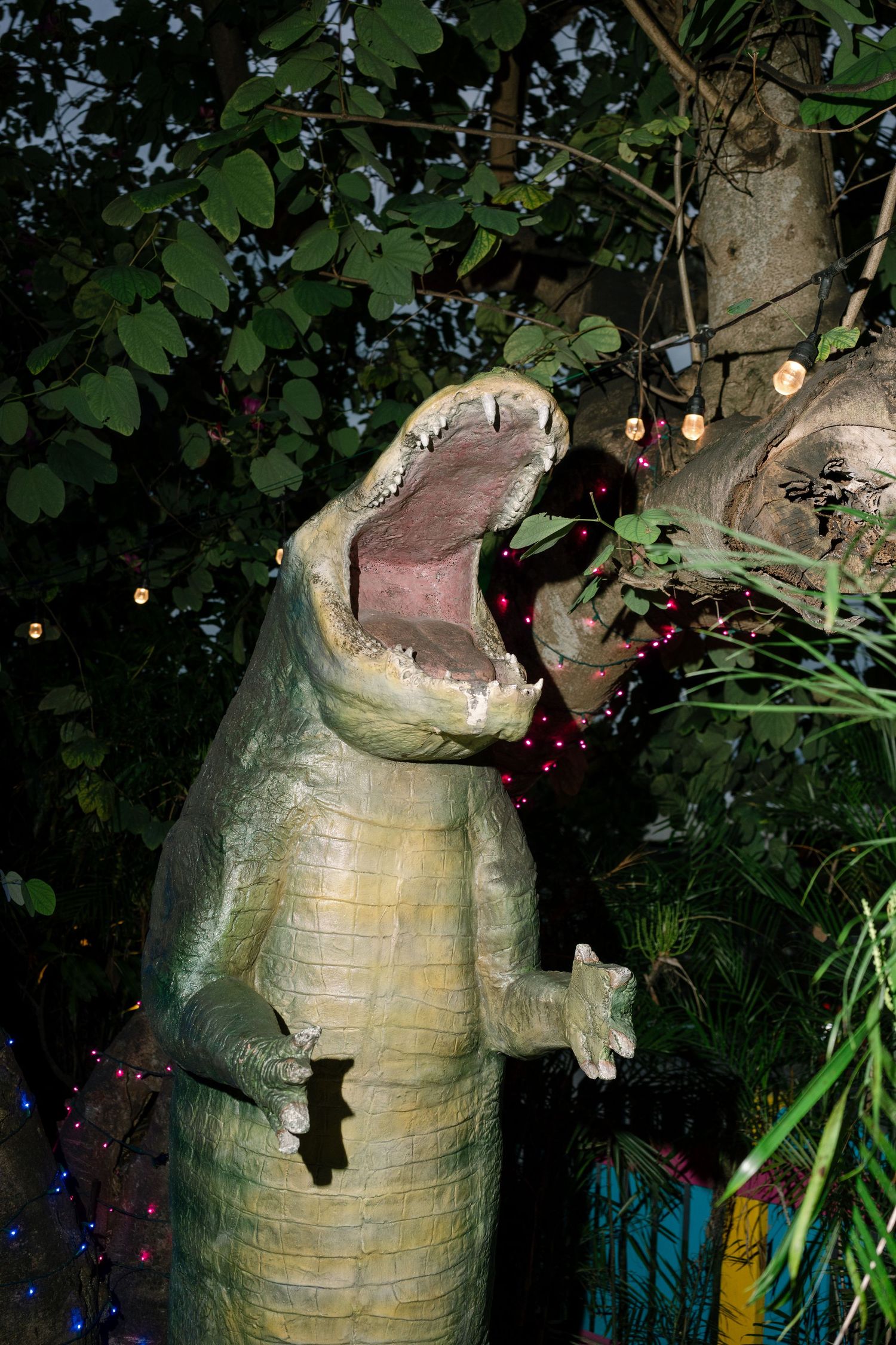 Large decorative dinosaur sculpture with open mouth illuminated at night in a garden setting.