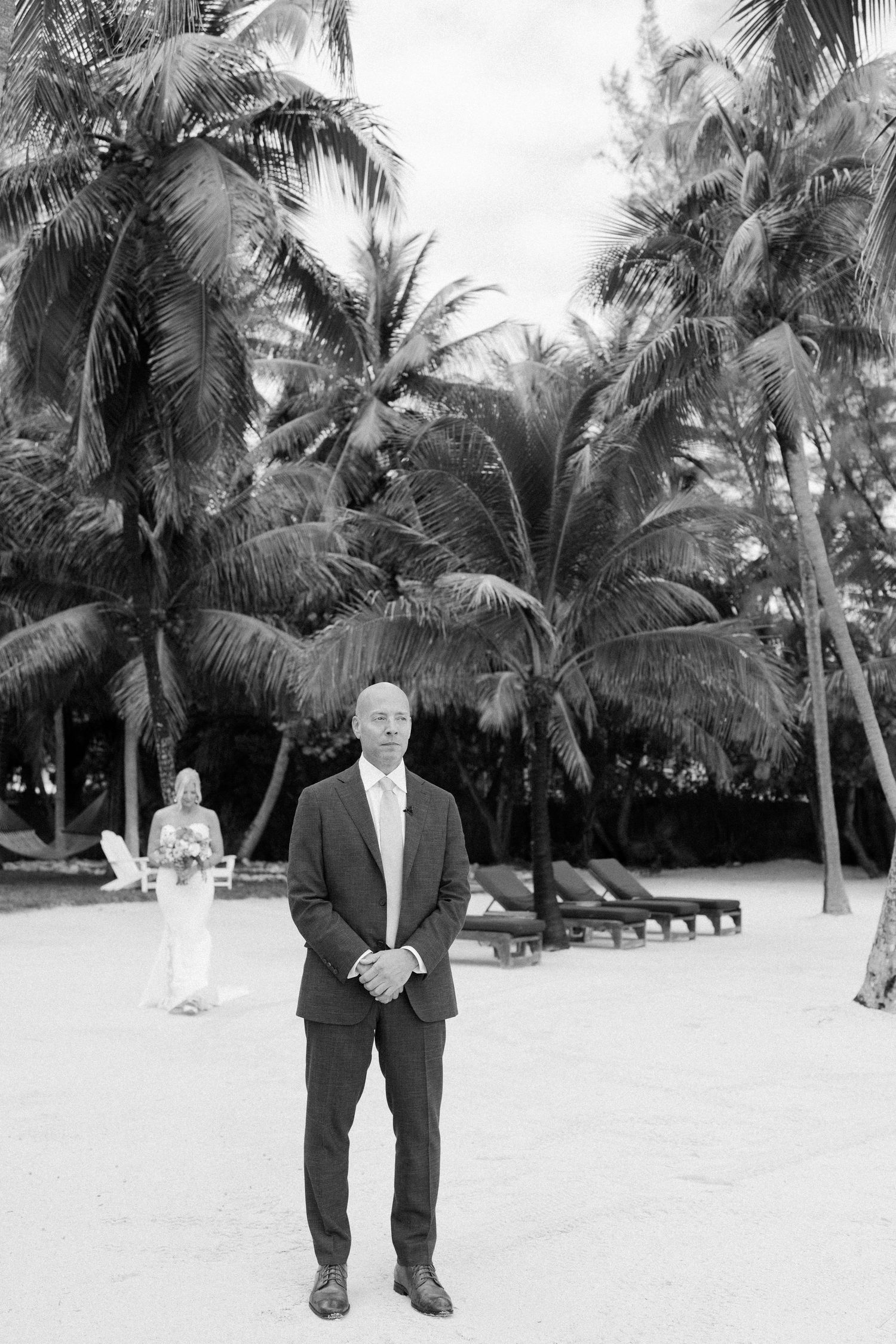 A formal portrait taken on a tropical beach with palm trees and lounge chairs in the background.
