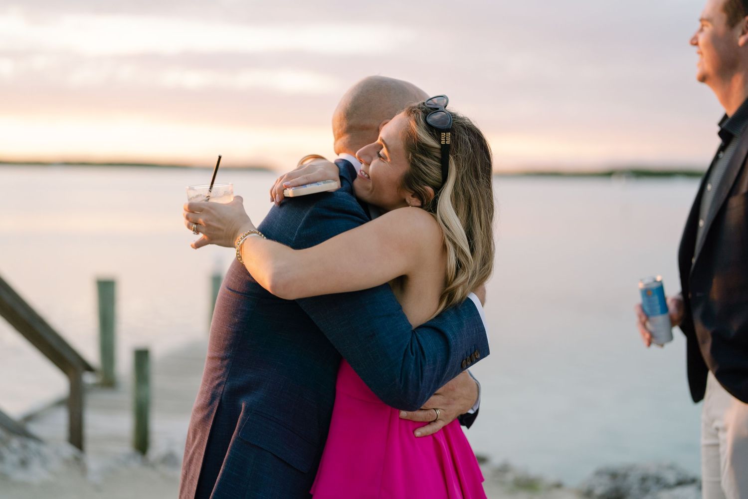 Guests share warm embraces during sunset at a waterfront celebration.