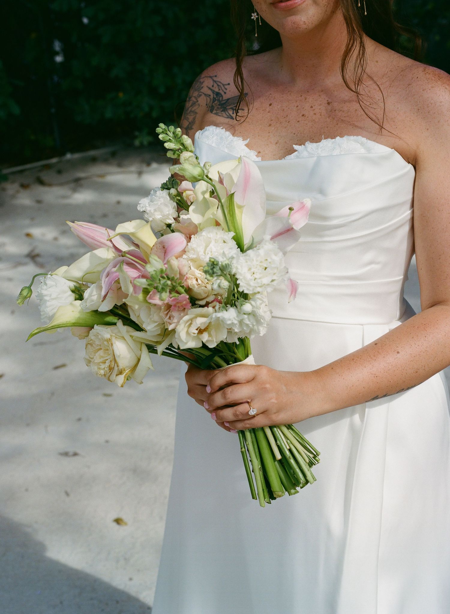 Bride in strapless white gown holds elegant bouquet of white and pink flowers with greenery.