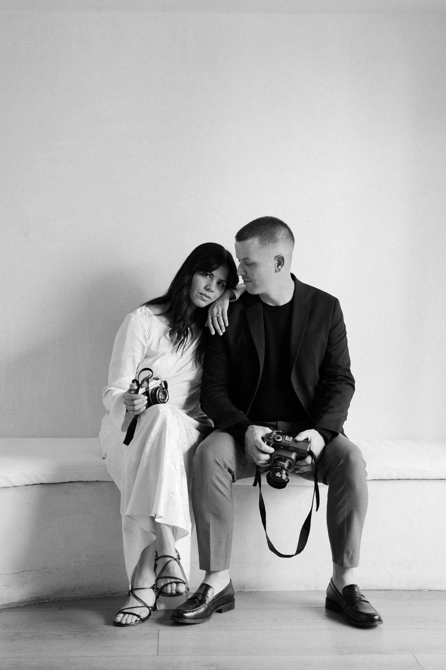 Two people in contrasting black and white outfits examining cameras while sitting on the floor.
