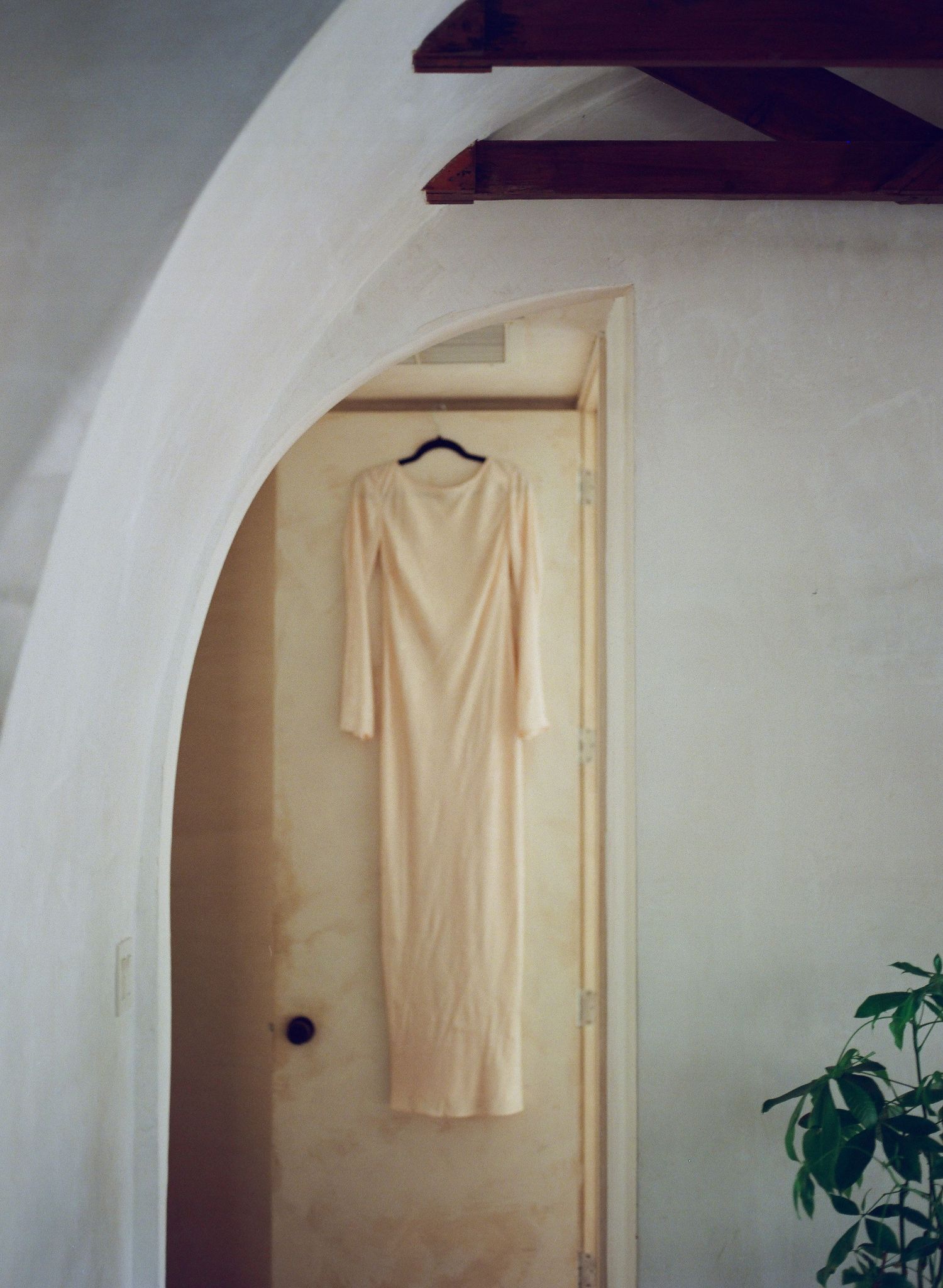 A white garment hangs on display against a minimalist white wall with an arched doorway.