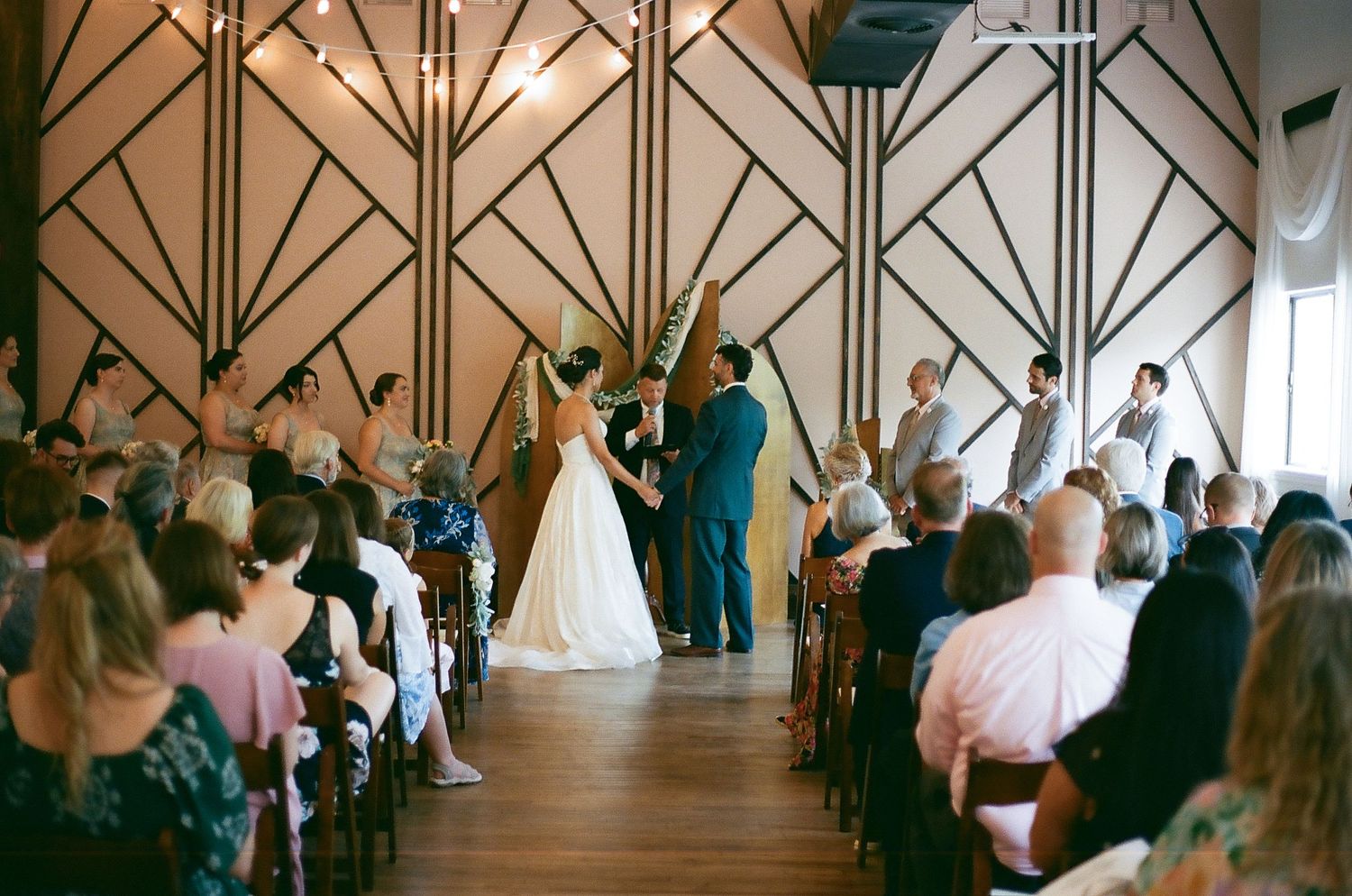 Wide view of wedding guests seated in a chapel with dramatic angular architectural details.