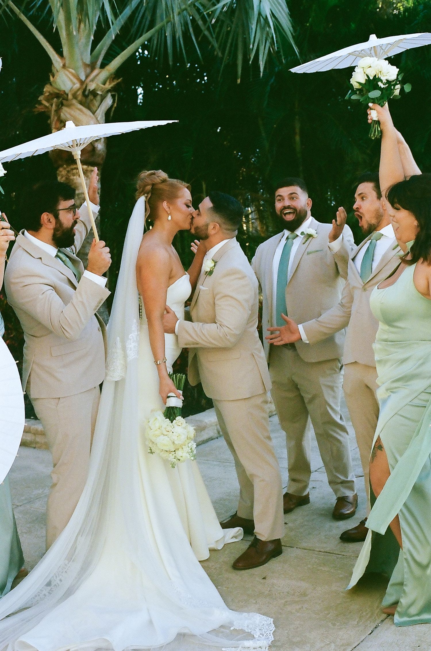Wedding party in beige and white attire poses together in a romantic outdoor setting.