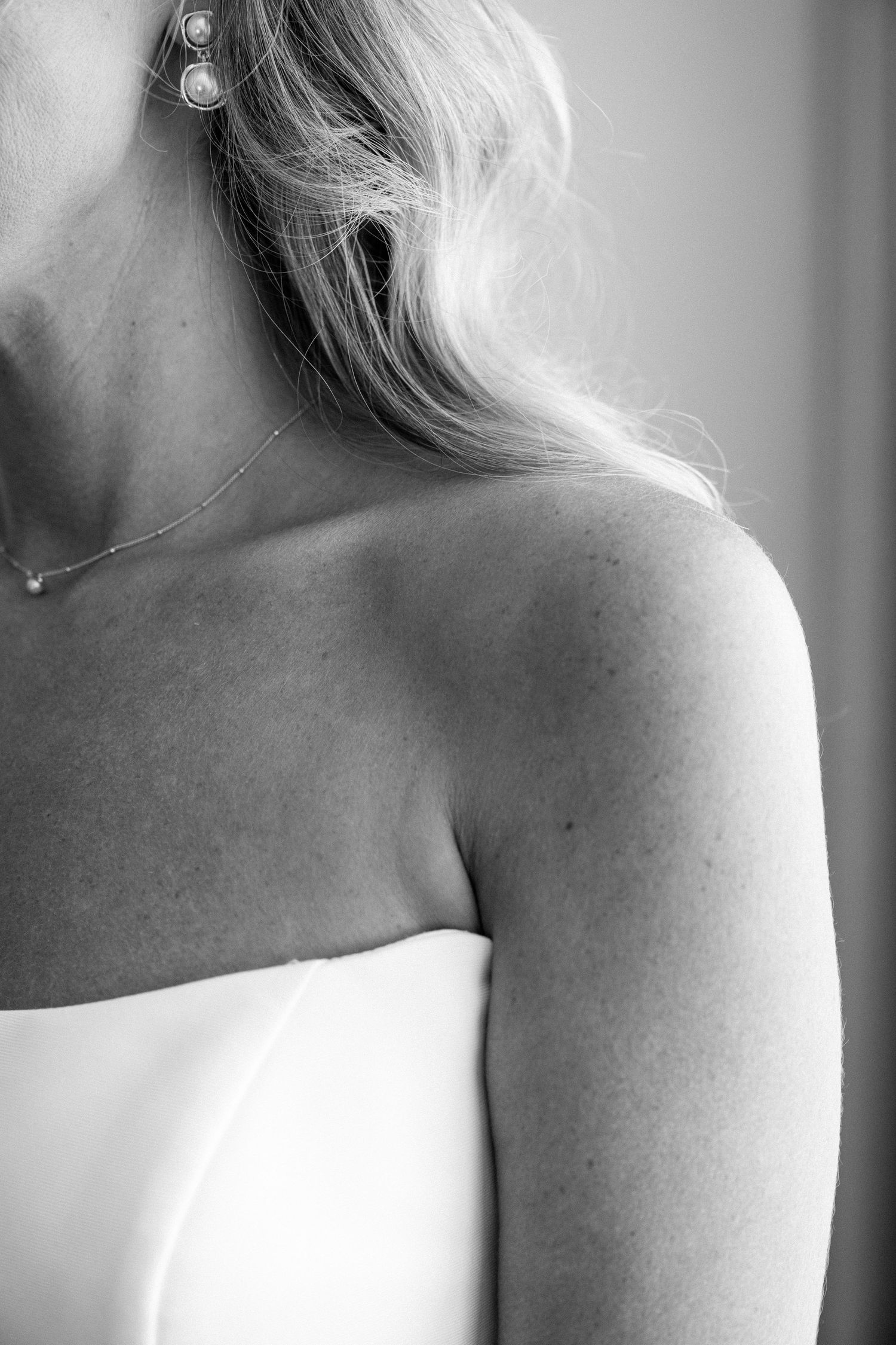 Close-up black and white photograph showing a delicate necklace and strapless white dress detail.