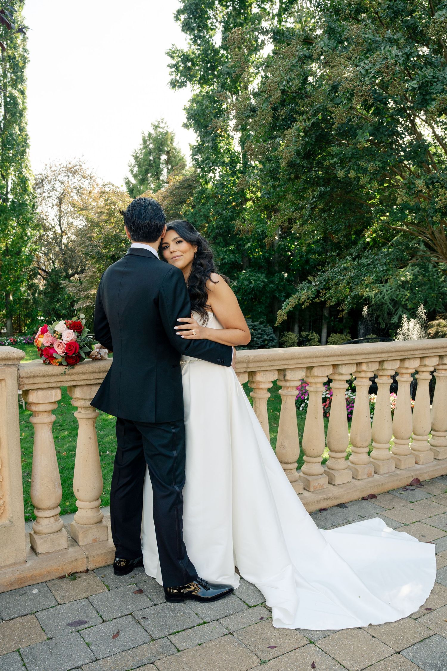 A wedding couple shares an intimate moment on a stone balcony surrounded by lush greenery.