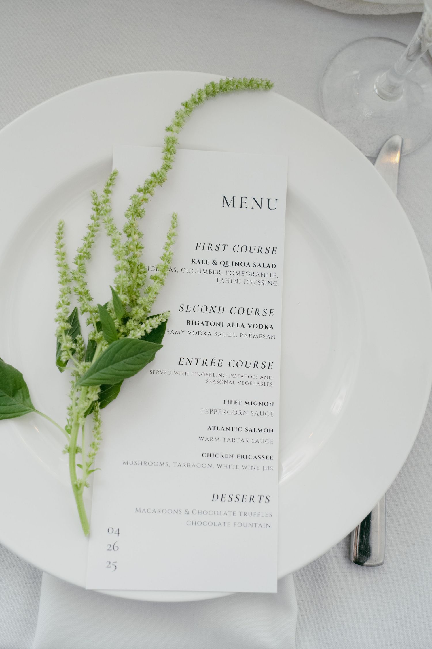 Elegant white menu cards with delicate green foliage accents on a light tablecloth.