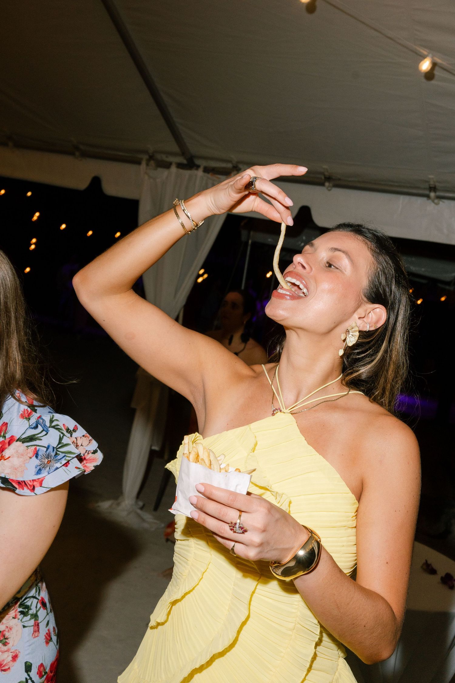 A woman in a yellow dress is seen dancing and celebrating at an outdoor event.