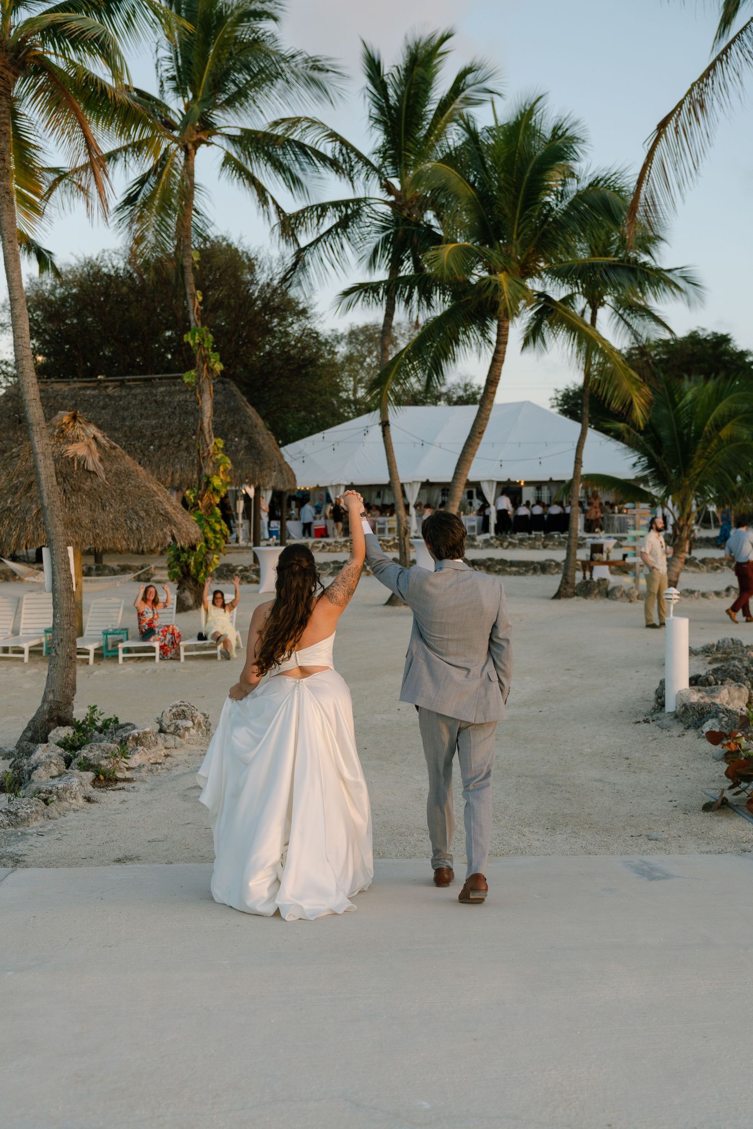 A bride and groom walking together on a tropical beach, surrounded by palm trees.
