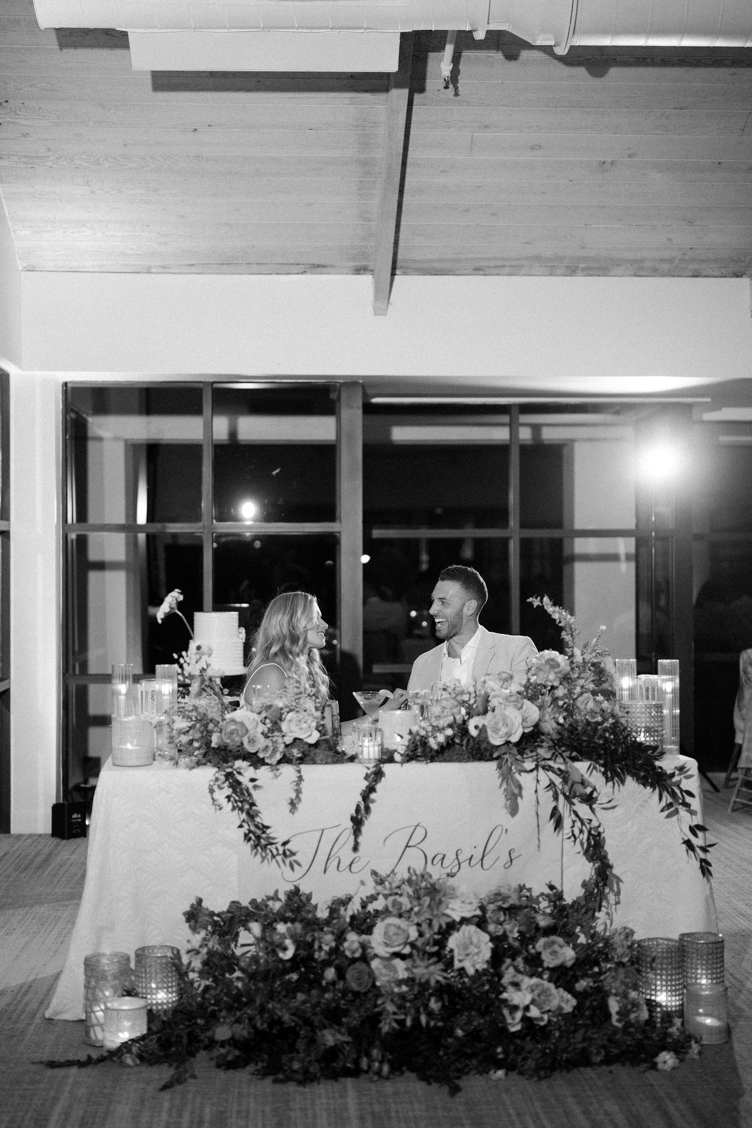 Wedding reception head table decorated with lush floral arrangements in black and white.