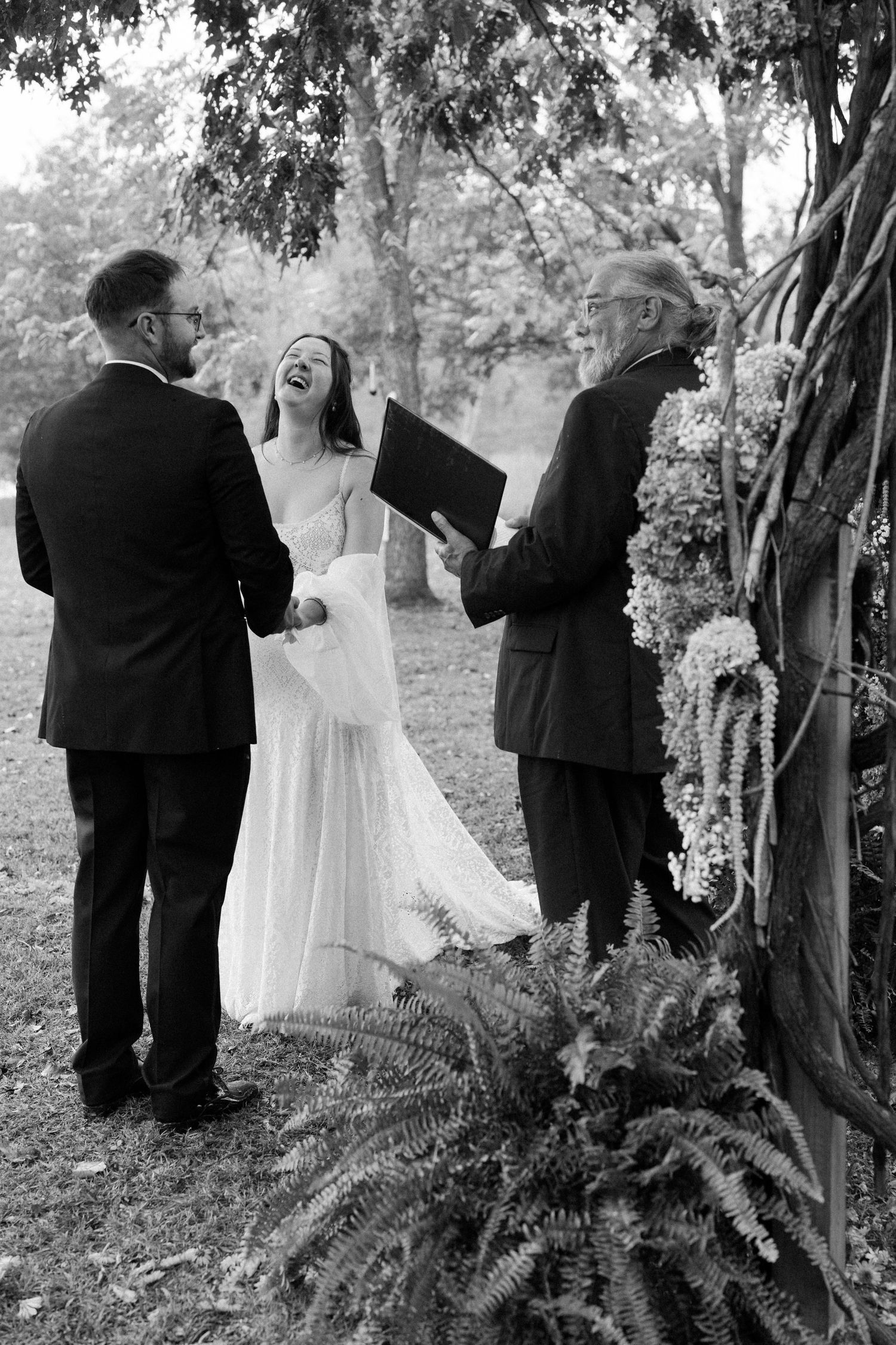A candid black and white photo sequence showing joyful laughter during an outdoor wedding ceremony among trees.
