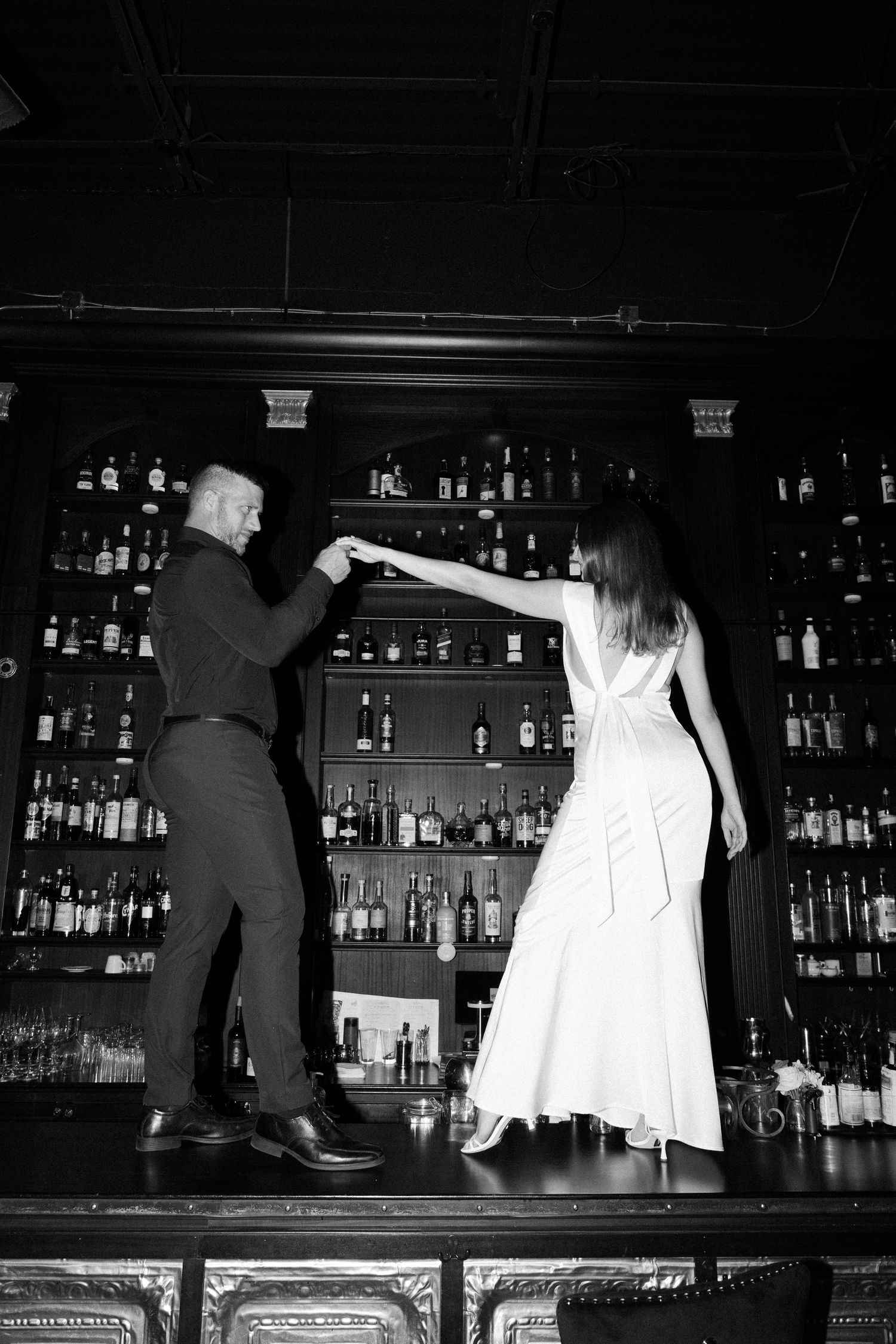 Black and white image sequence showing a bartender working behind a bar counter with bottles visible in the background.