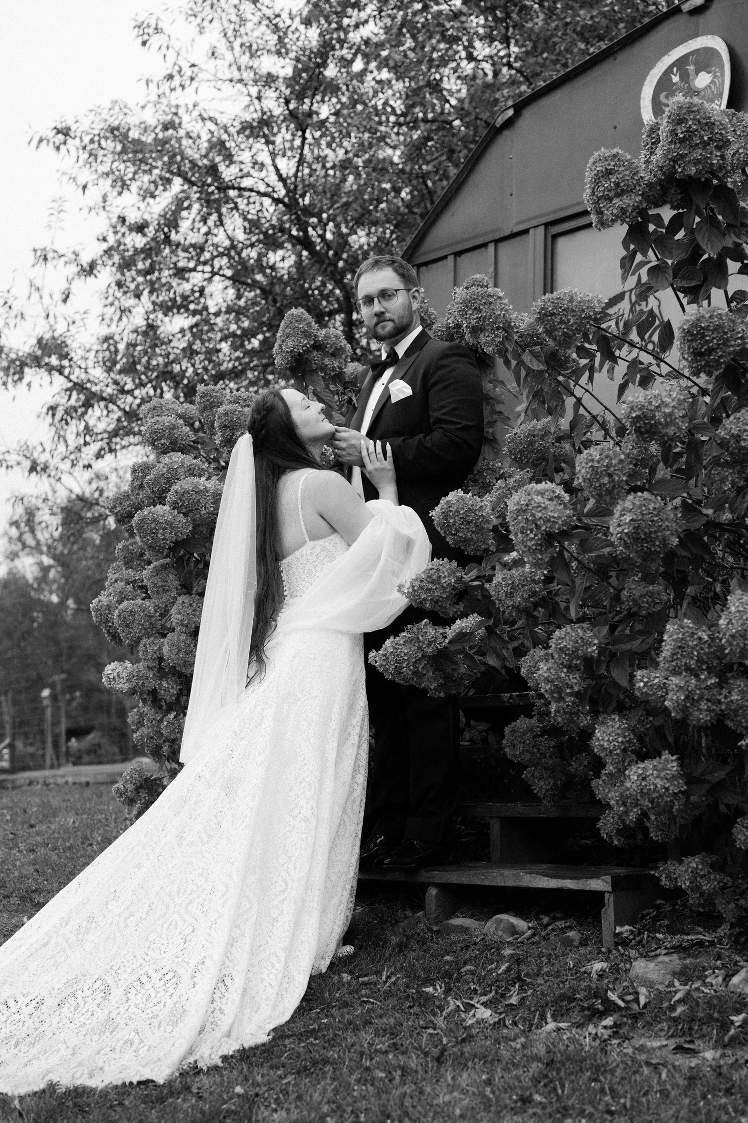 A romantic black and white wedding photo captured in front of a blooming hydrangea bush.