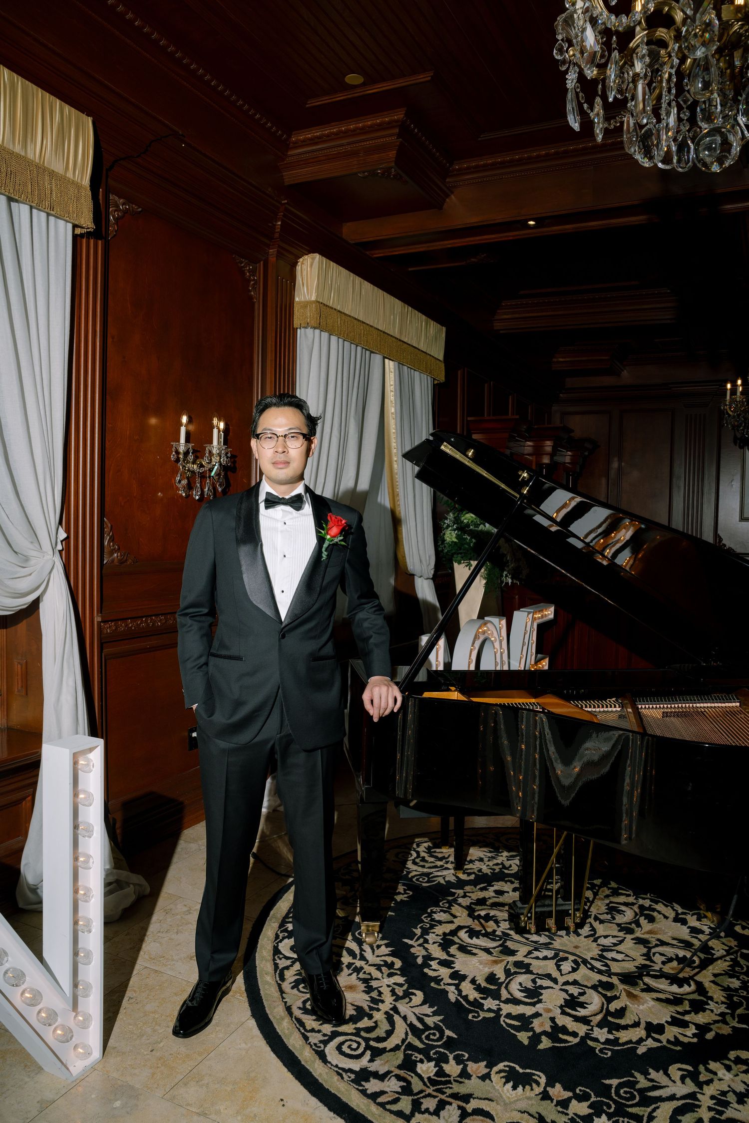 Elegant formal event setting with black tuxedo and ornate carpet in a room with chandeliers and piano.