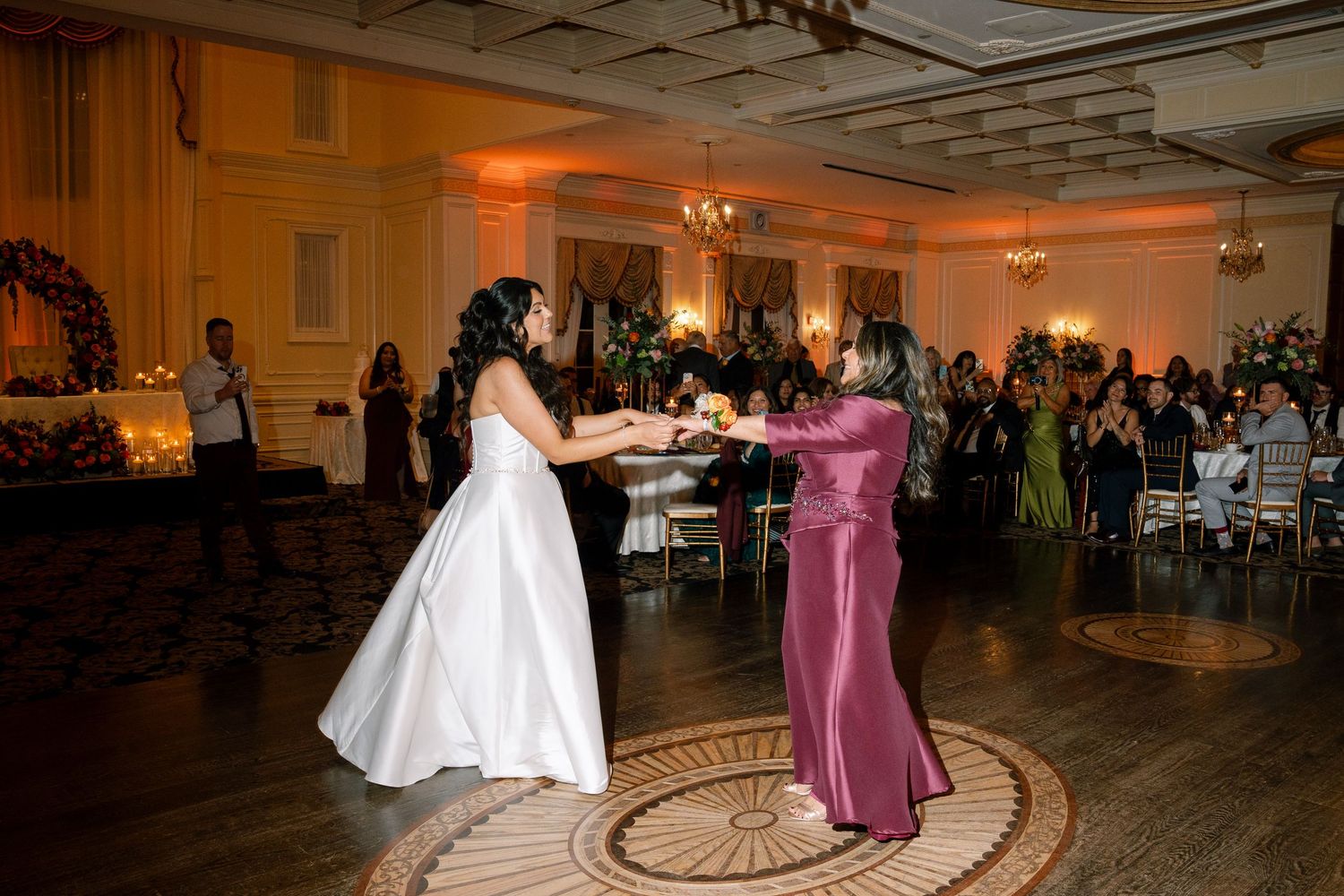 Wedding reception dance floor scene with amber uplighting and guests celebrating in an elegant ballroom.